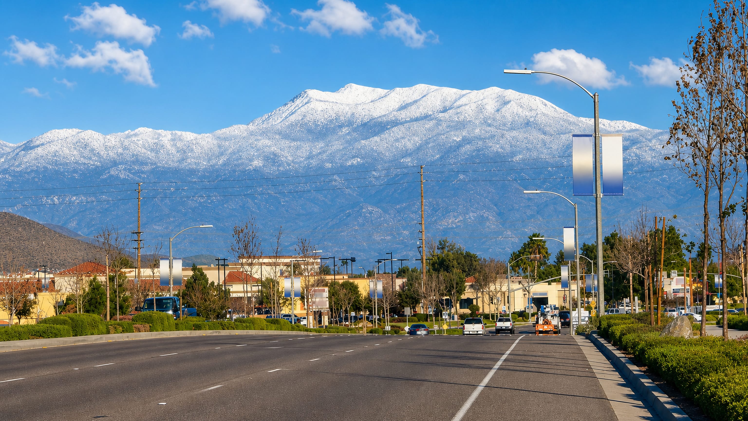 Wide boulevard through Menifee, California, lined with low retail buildings below snow-dusted mountains.