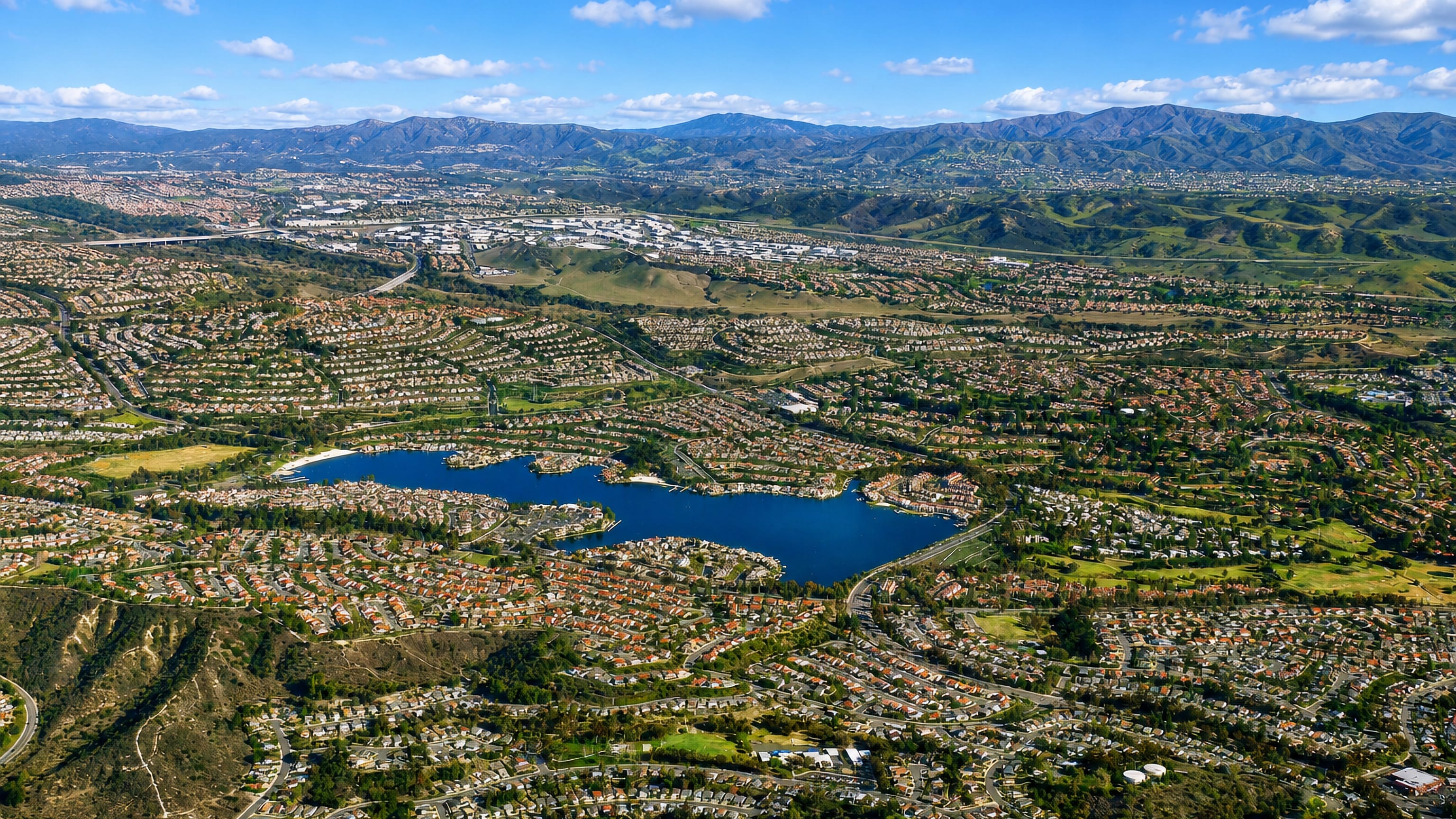 Aerial of Mission Viejo, California, its lake ringed by tile-roofed suburbs below the Santa Ana Mountains.