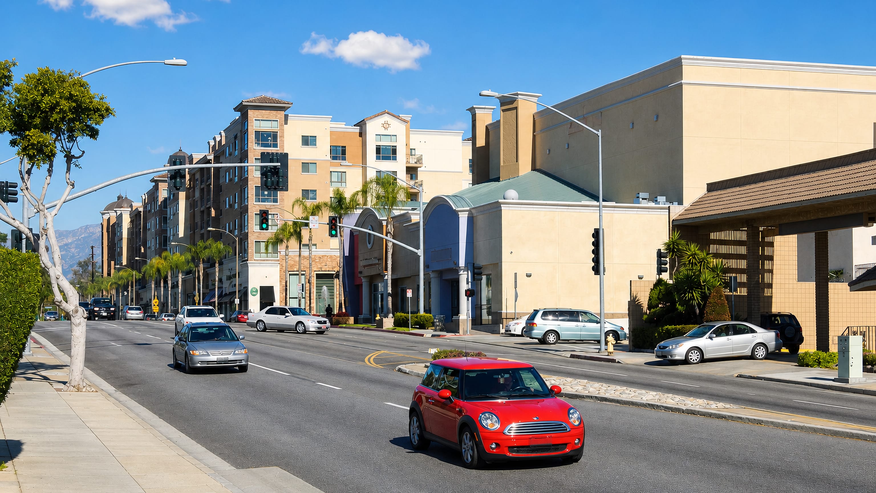 Wide boulevard with stucco mixed-use blocks and palms in Monterey Park, California, below the San Gabriel Mountains.