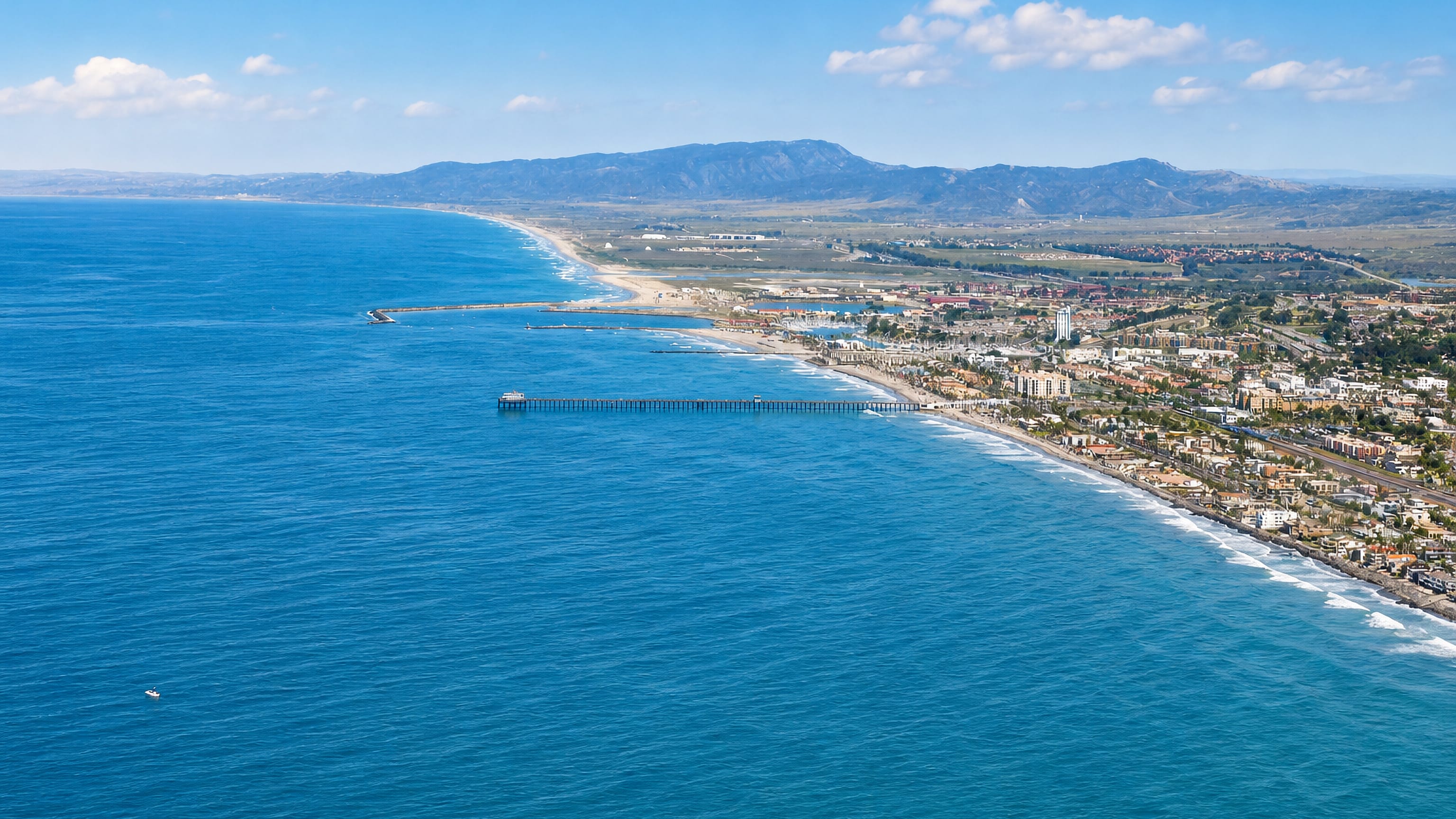 Aerial view of Oceanside, California, with its long wooden pier, beach, harbour jetties and coastal hills.