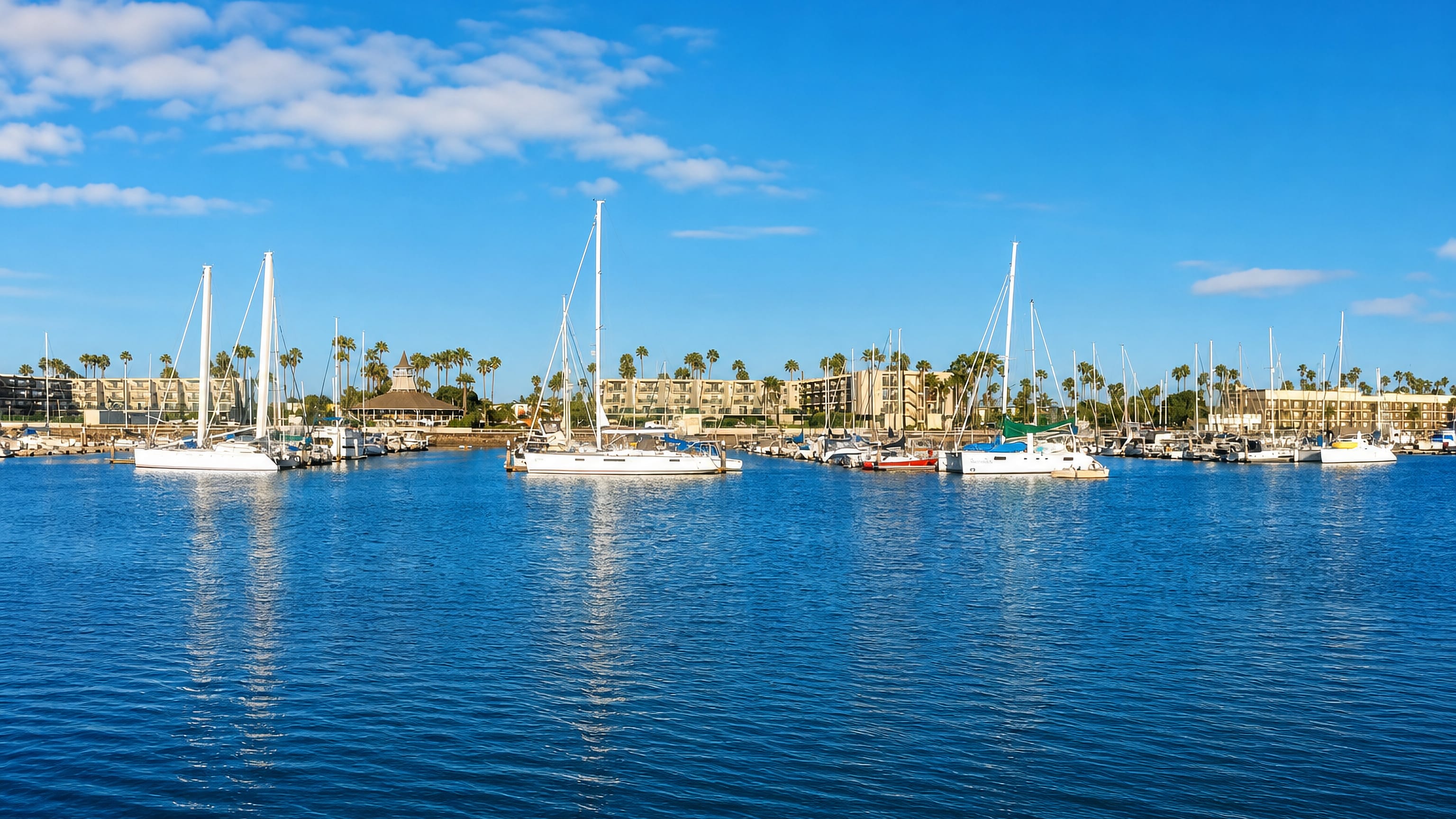 Sailboats moored at Channel Islands Harbor in Oxnard, with palm-lined condominiums along the shore.