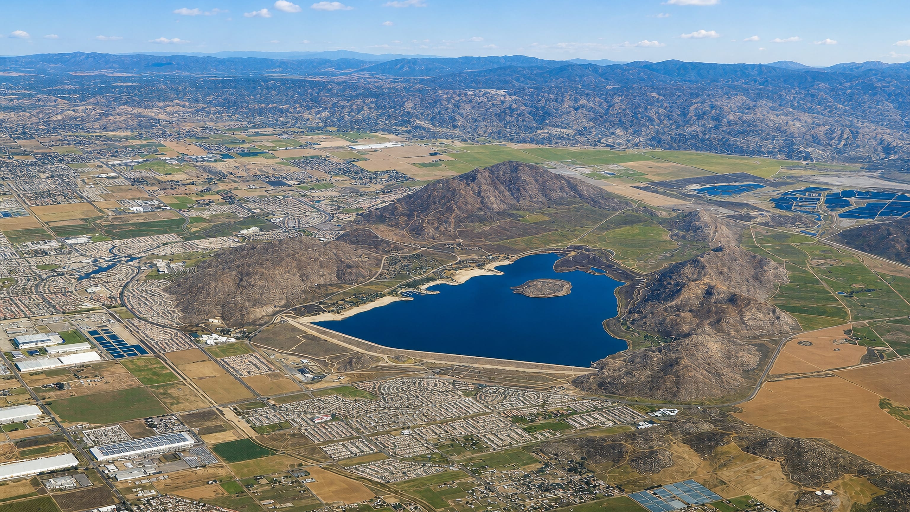 Aerial of Perris, California, with Lake Perris and rocky hills above the valley's spreading suburbs.