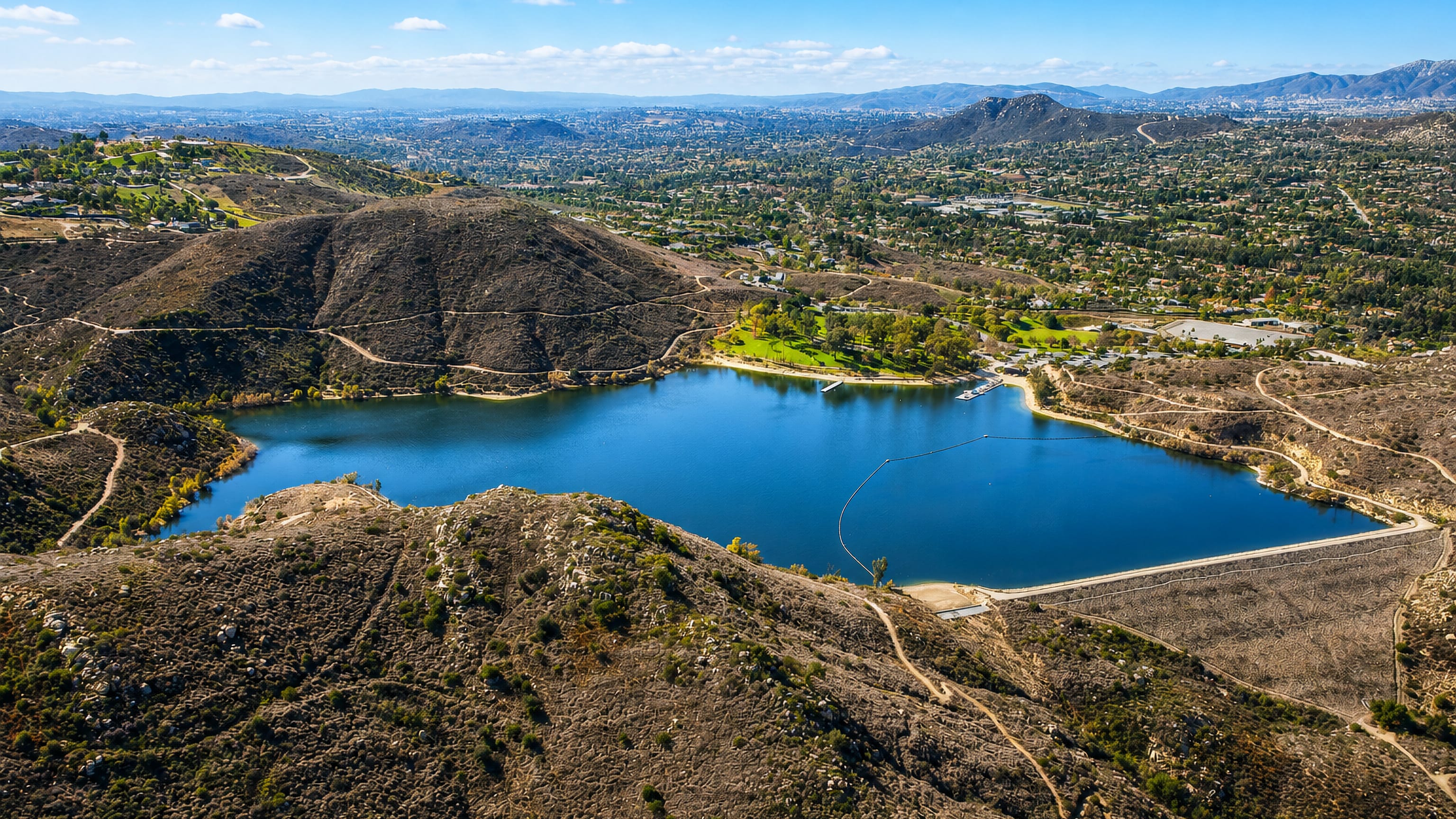 Aerial view of Lake Poway reservoir and its dam ringed by chaparral hills and the suburbs of Poway, California.