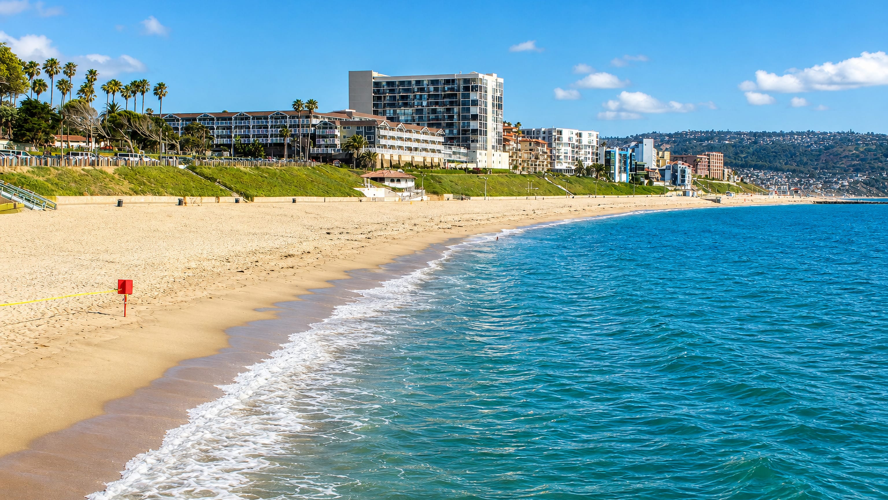 Curving sandy beach, blue Pacific surf and bluff-top apartment blocks along Redondo Beach, California.