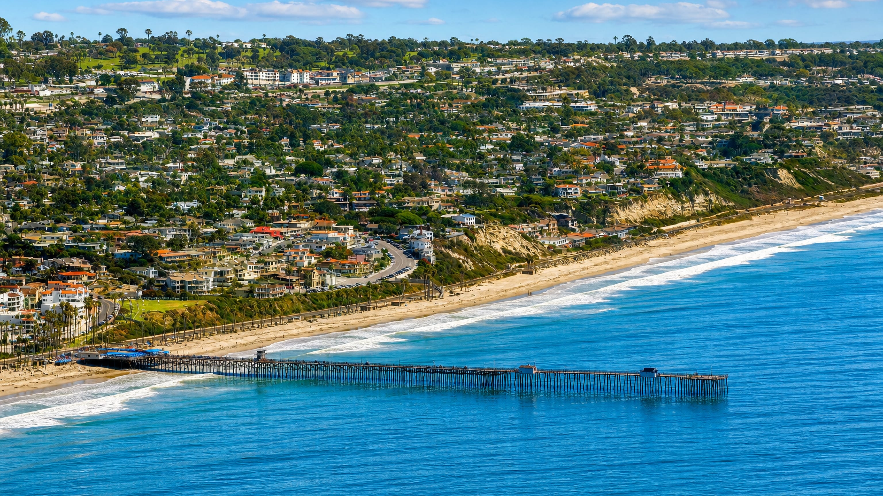 San Clemente's wooden pier, wide beach and hillside Spanish-tiled homes above the Pacific in California.