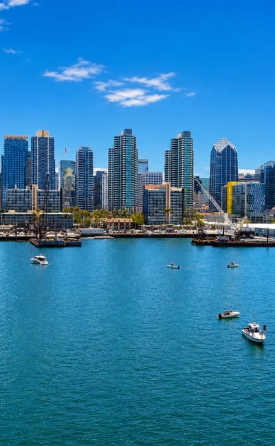 San Diego's downtown skyline across the harbor with sailboats and a tall ship on the bay.