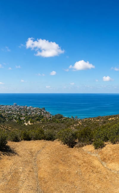Panoramic coastal view over La Jolla and the Pacific Ocean from a hilltop trail with a lookout bench in San Diego.