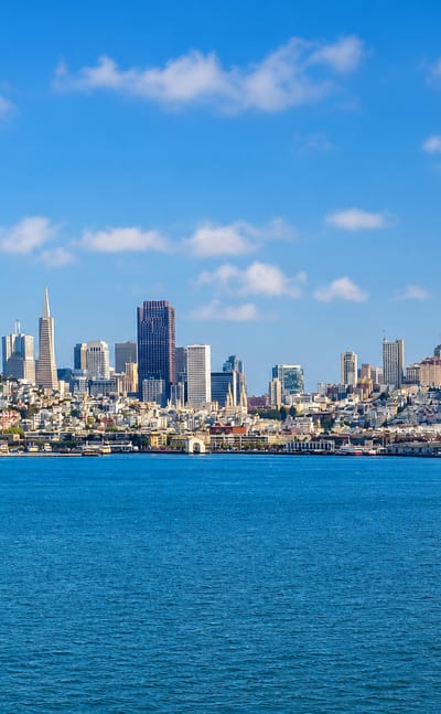 San Francisco skyline across the bay with Salesforce Tower and the Transamerica Pyramid under blue sky.