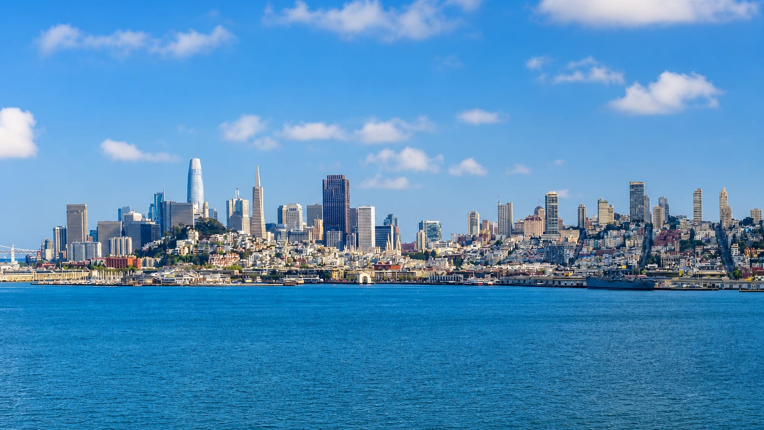 San Francisco skyline across the bay with Salesforce Tower and the Transamerica Pyramid under blue sky.