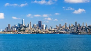 San Francisco skyline across the bay with Salesforce Tower and the Transamerica Pyramid under blue sky.
