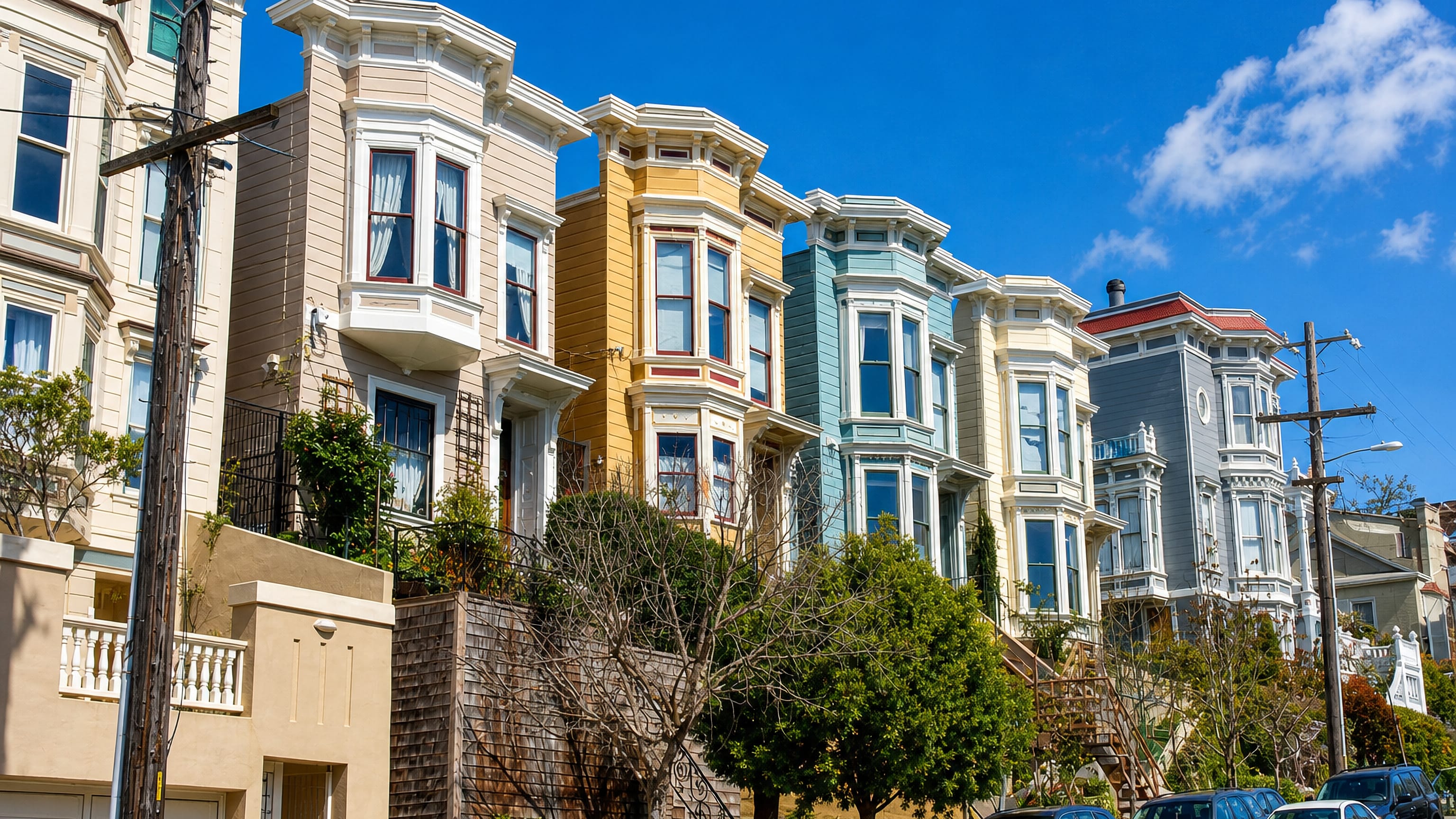 A hillside row of pastel Victorian bay-window houses on a Noe Valley street in San Francisco.