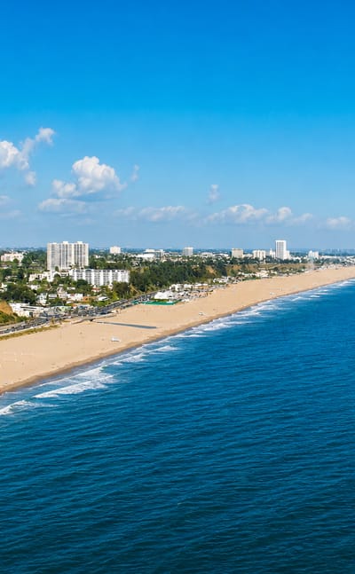 Aerial view of Santa Monica's sweeping sandy beach, coastal bluffs and low-rise skyline along the Pacific.