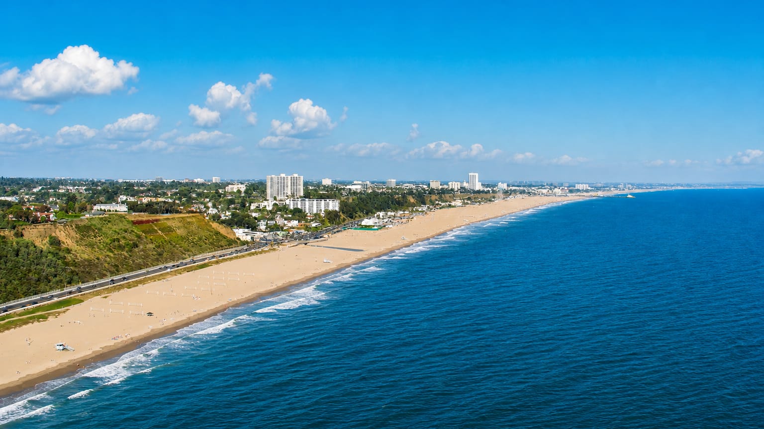 Aerial view of Santa Monica's sweeping sandy beach, coastal bluffs and low-rise skyline along the Pacific.