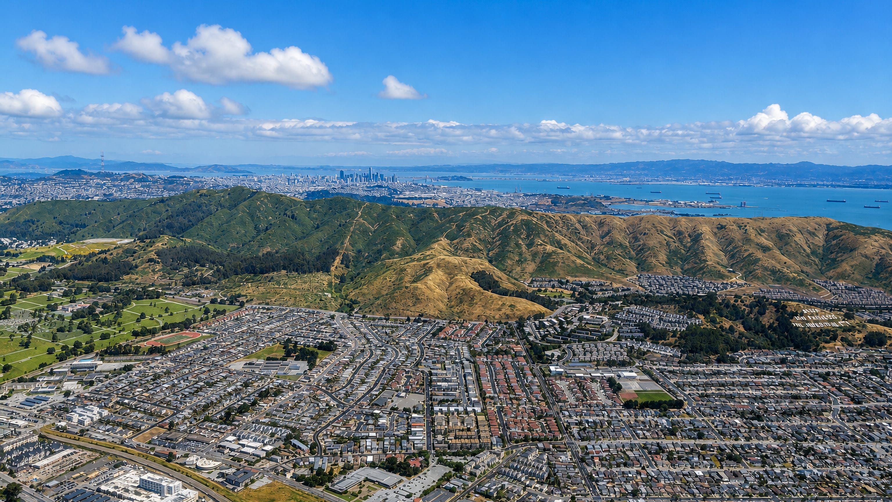 Aerial view over South San Francisco's hillside neighbourhoods toward San Bruno Mountain, the bay and the SF skyline.