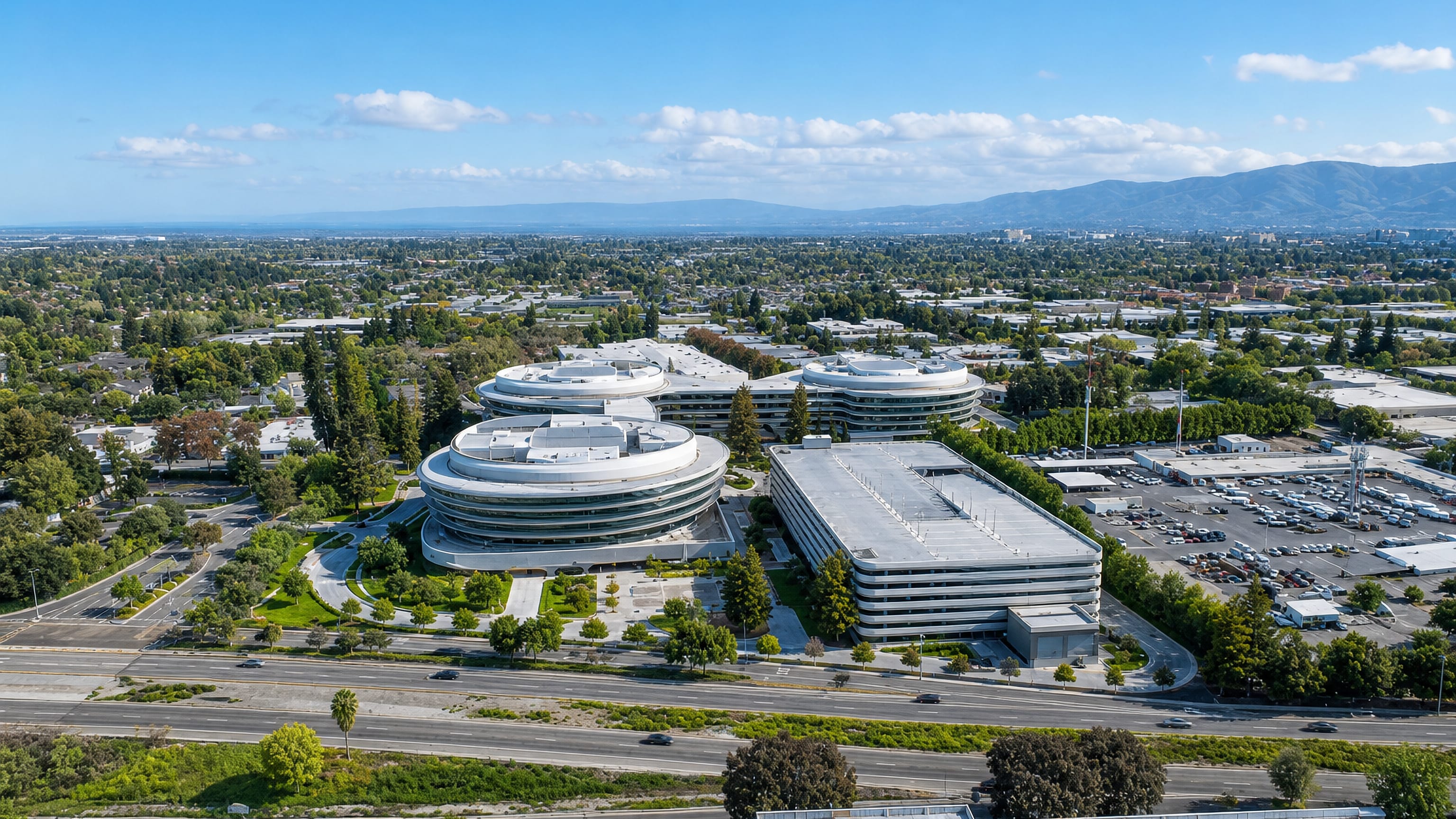 Aerial view of Sunnyvale's curved tech-campus offices, expressway and low sprawl below the distant Diablo hills.