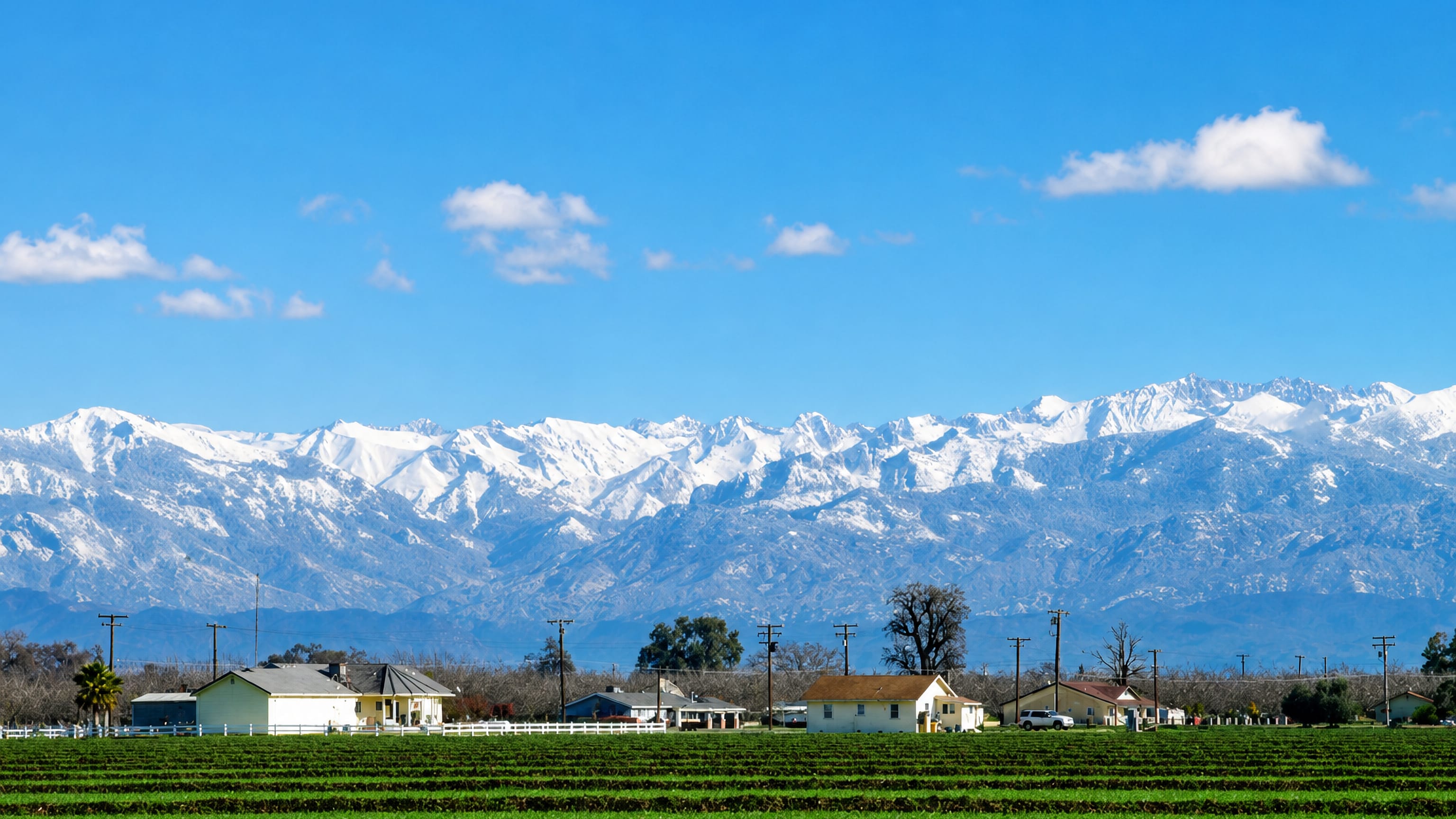 Farm rows and roadside houses below the snow-capped Sierra Nevada outside Tulare, California.