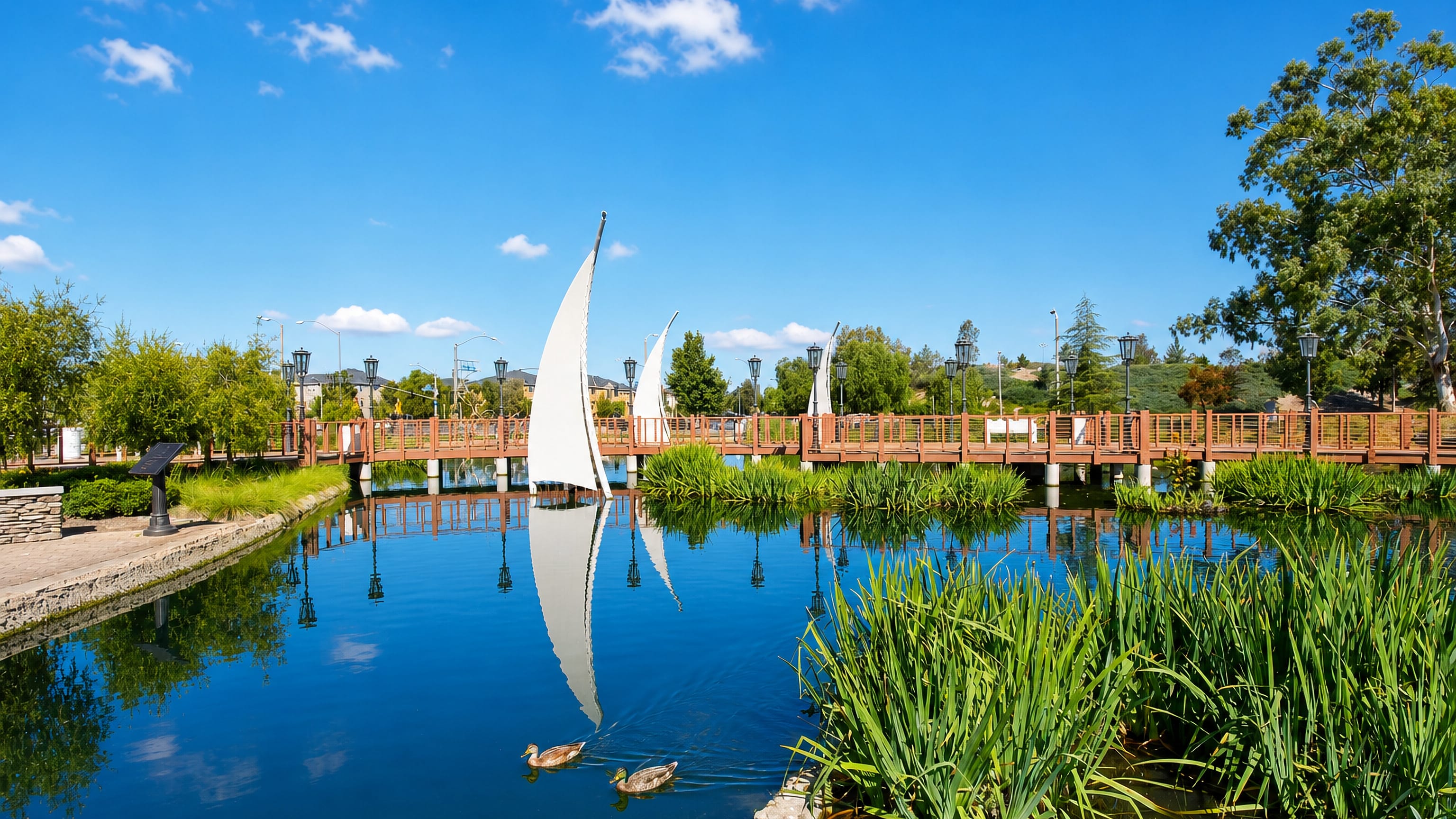 Wooden paseo bridge and white sail sculptures over a lake in Valencia, Santa Clarita, California.