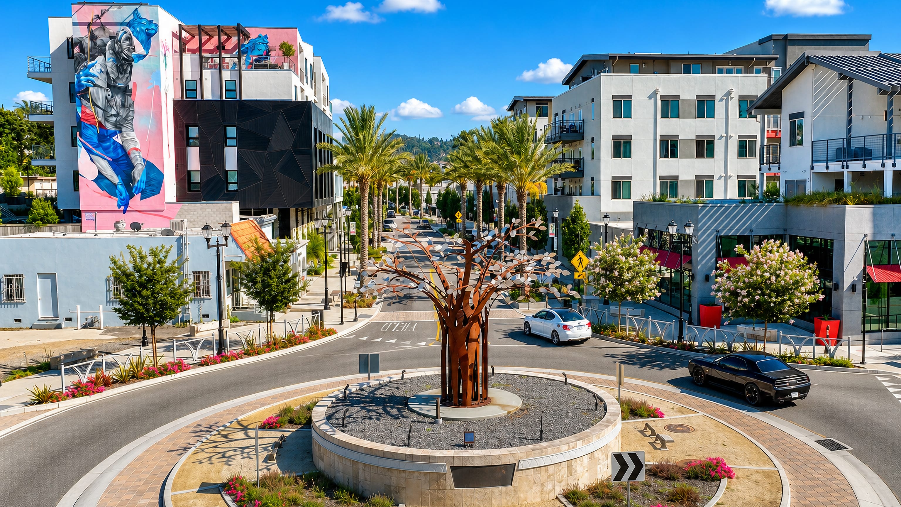 Downtown Vista, California: a steel tree sculpture roundabout, palm-lined street and a muralled mixed-use block
