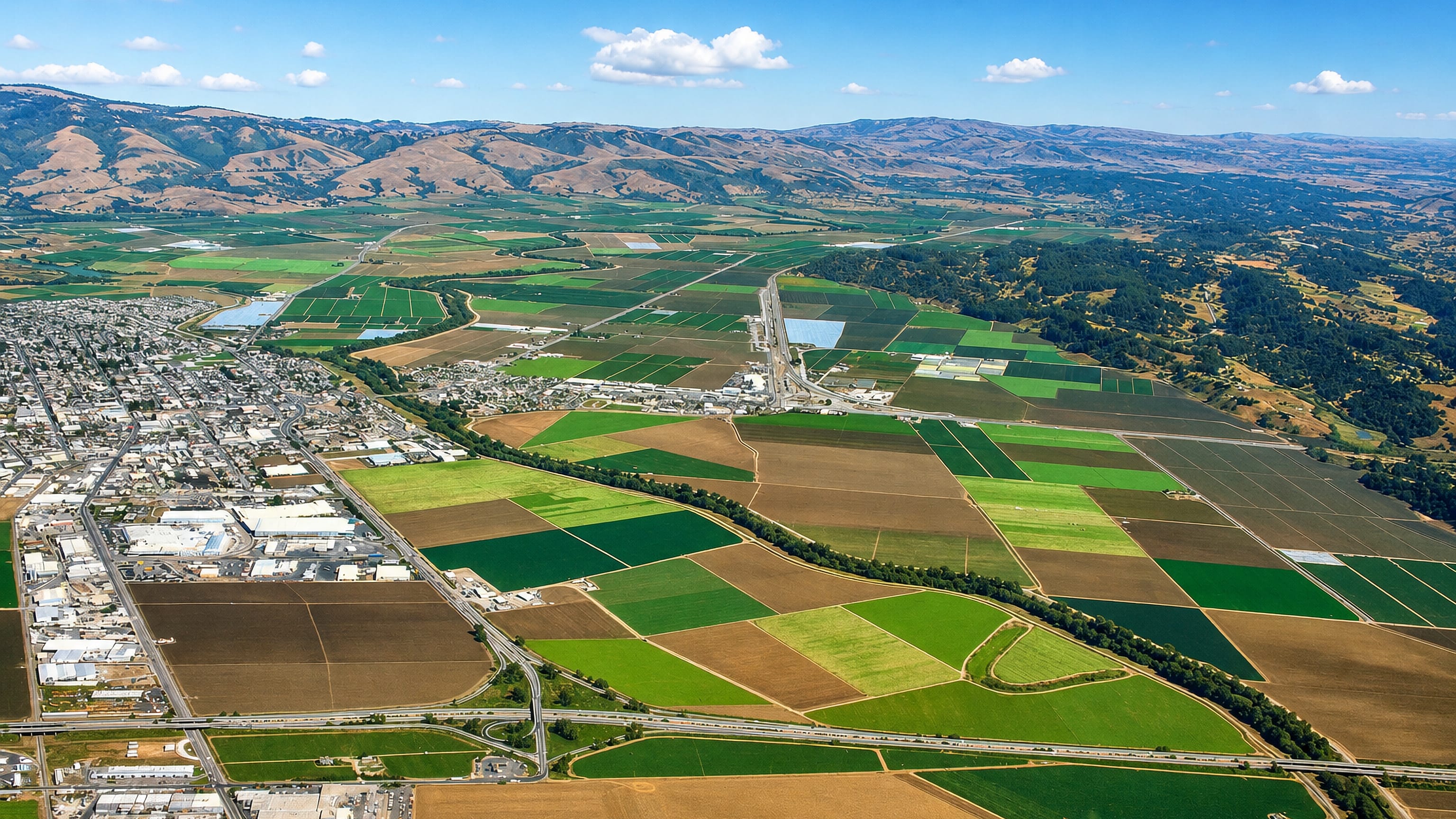 Aerial view of Watsonville, California, at the edge of Pajaro Valley farm fields with coastal hills beyond.