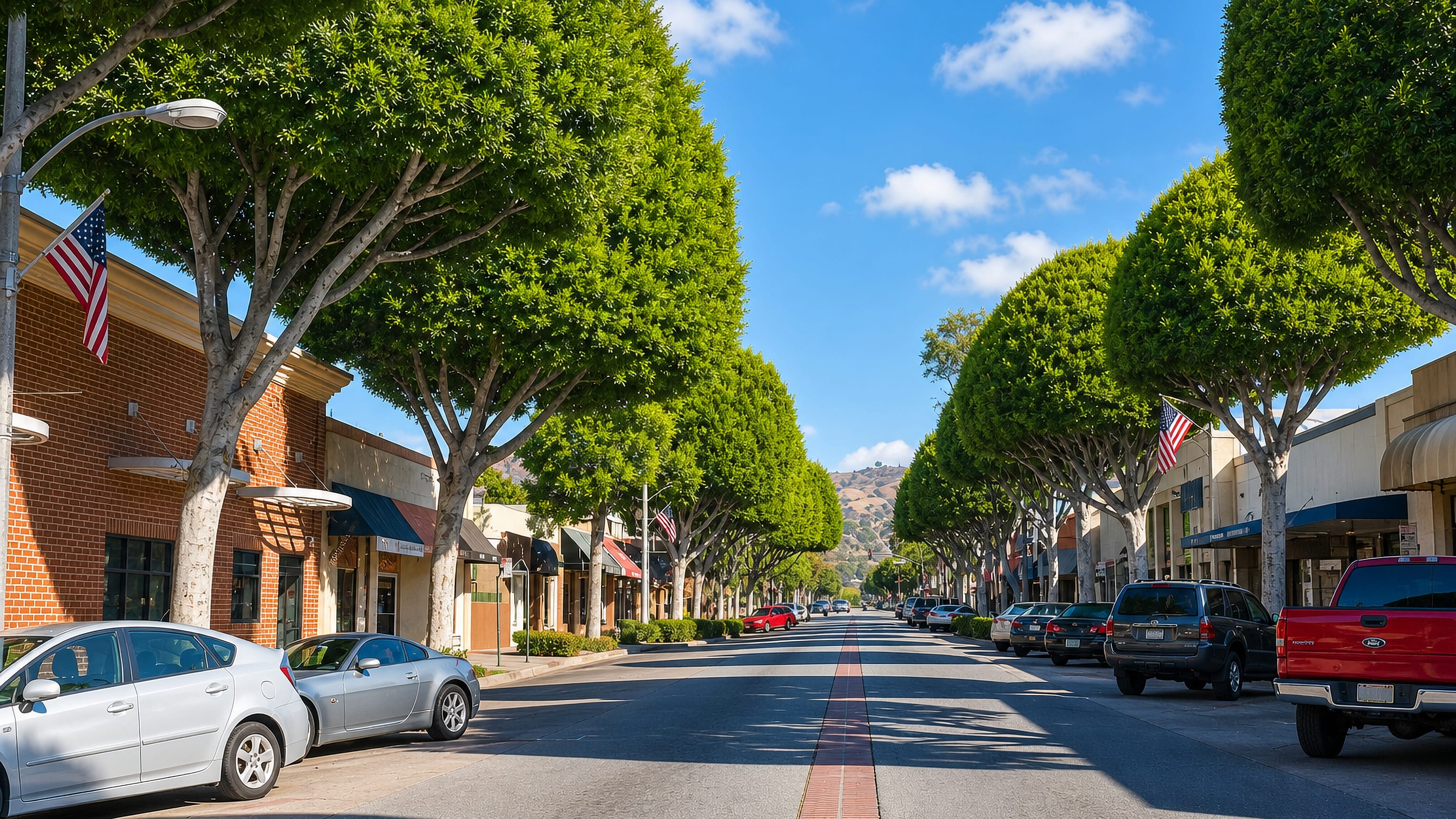 Tree-lined Greenleaf Avenue in Uptown Whittier, California, with brick storefronts, US flags and hills beyond.
