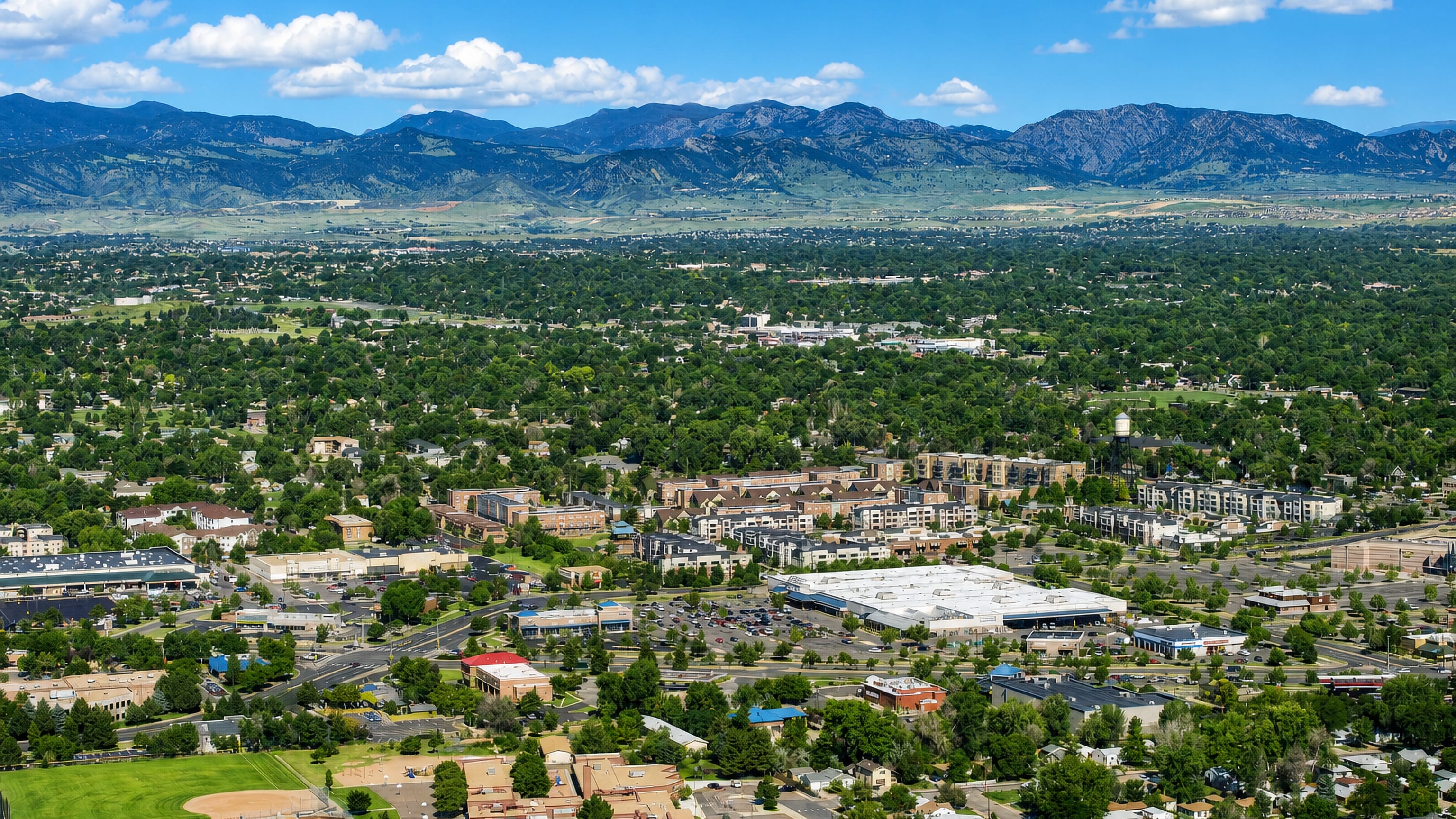 Arvada, Colorado, from above: leafy suburban streets and low commercial blocks below the Front Range foothills.