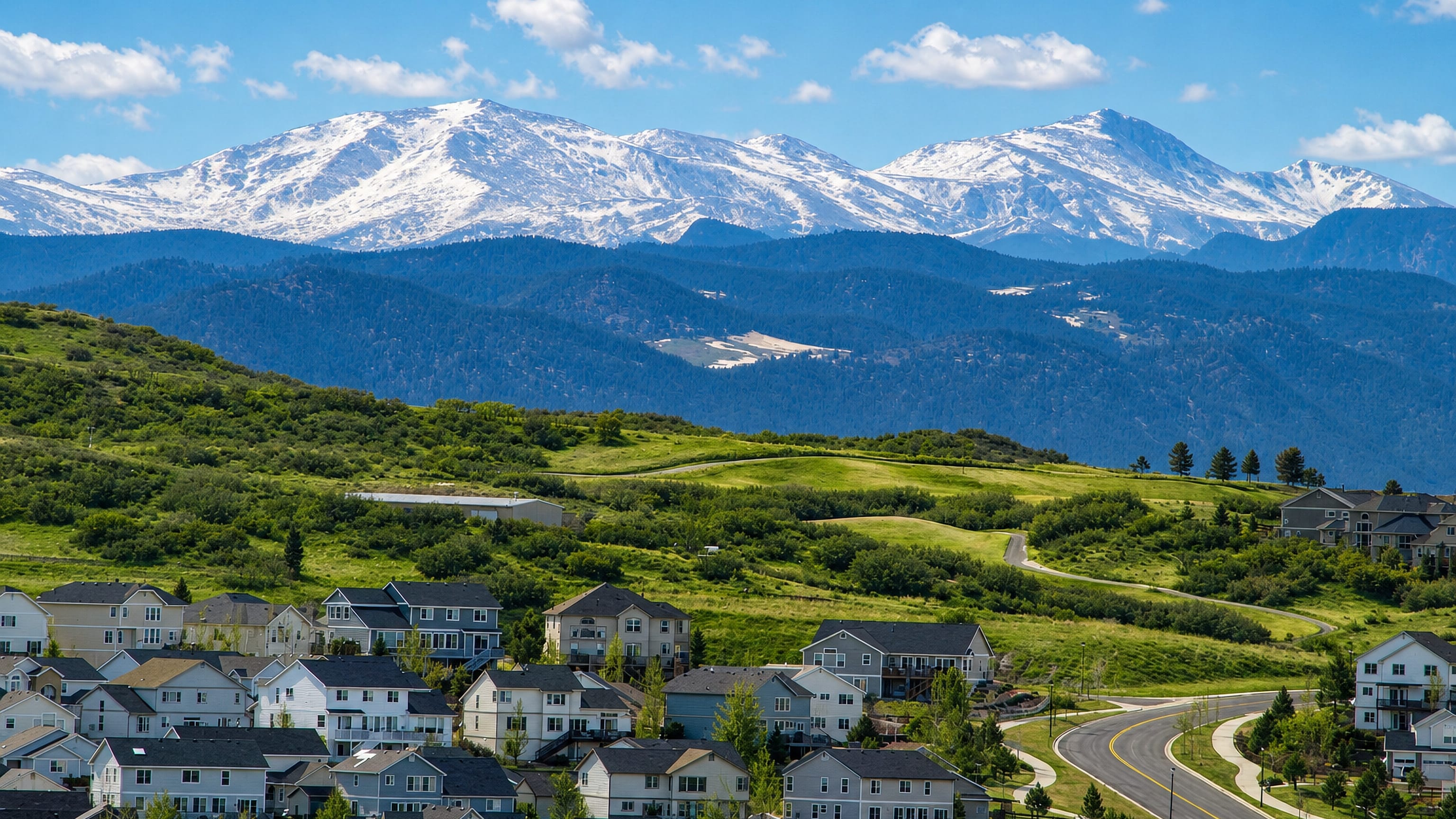 Hillside homes in Castle Rock, Colorado, above green meadows with the snow-capped Front Range on the horizon.