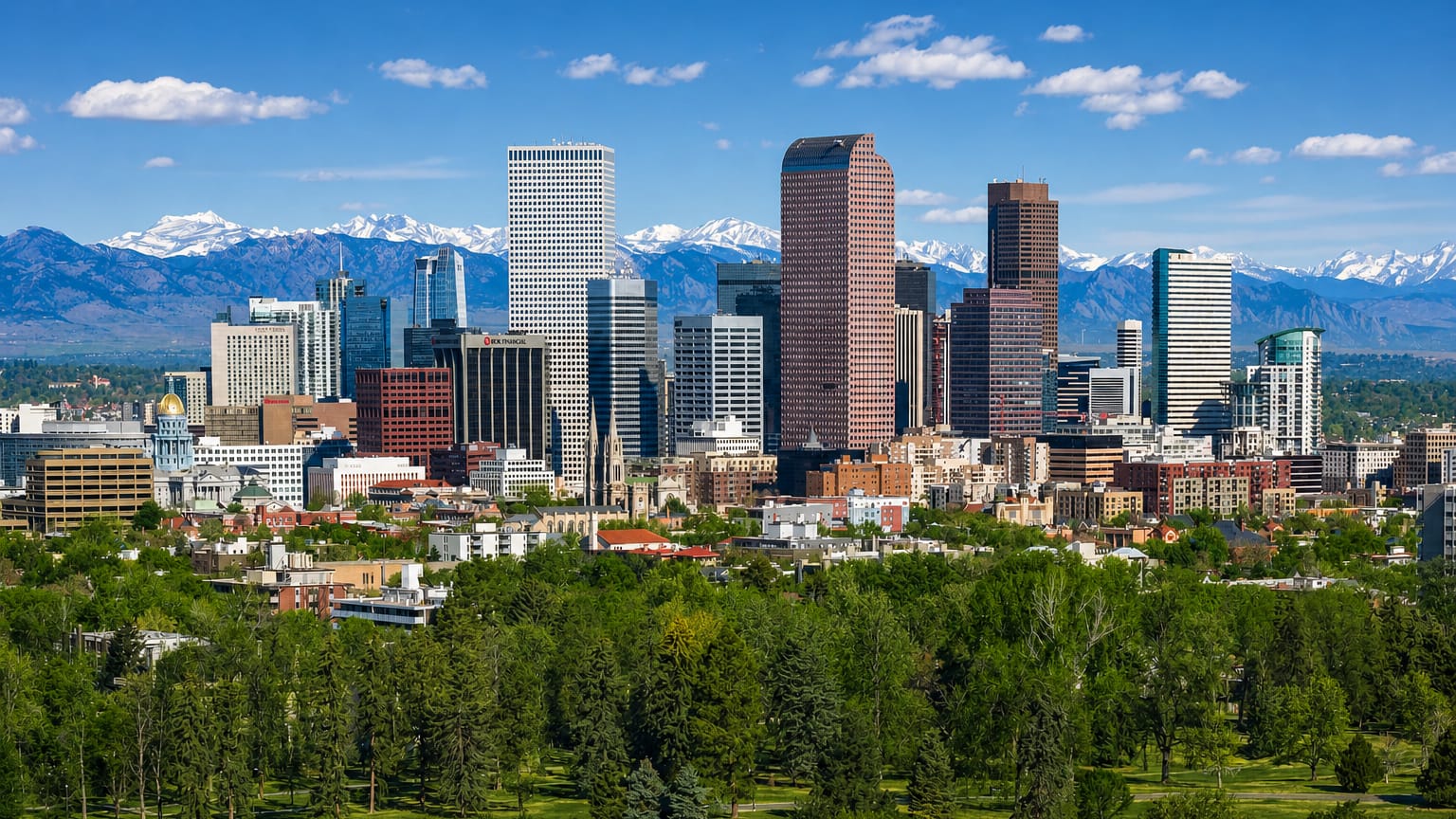 Denver's downtown skyline with the Rocky Mountains behind and a green park in the foreground.