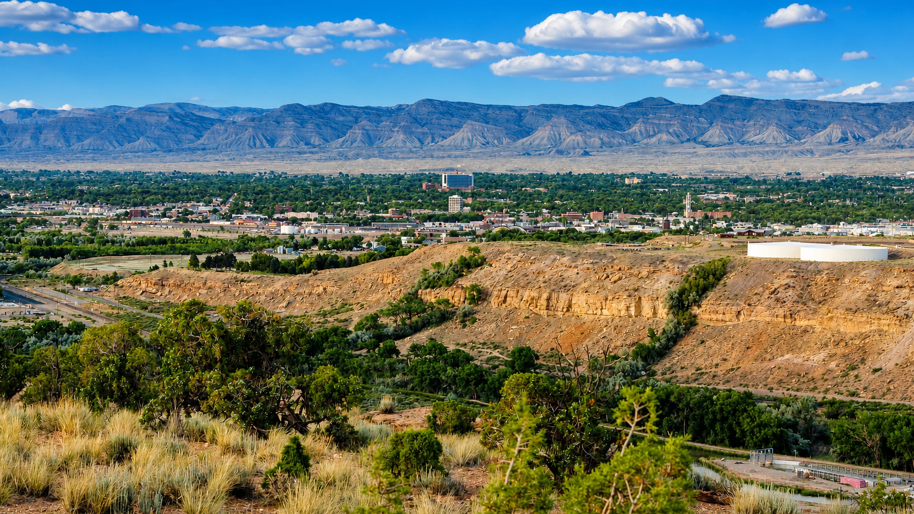 Downtown Grand Junction, Colorado spread below the Book Cliffs, with sandstone bluffs and sagebrush in the foreground