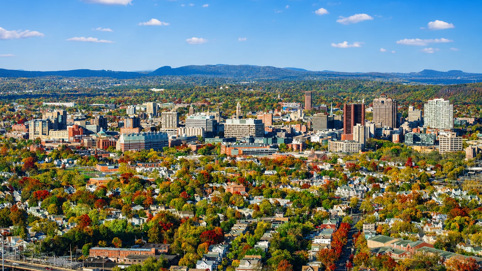 Aerial view of New Haven, Connecticut, downtown amid autumn foliage with traprock ridges in the distance.