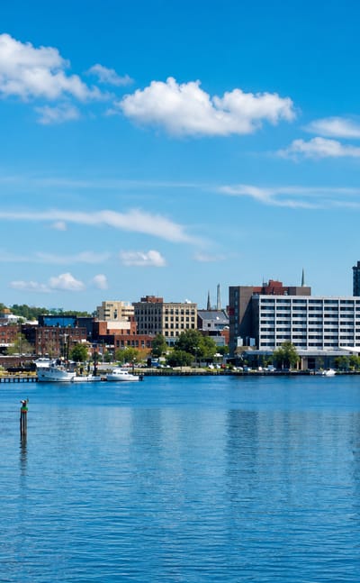 Waterfront skyline of Wilmington, Delaware, with mid-rise buildings and a marina along the river.