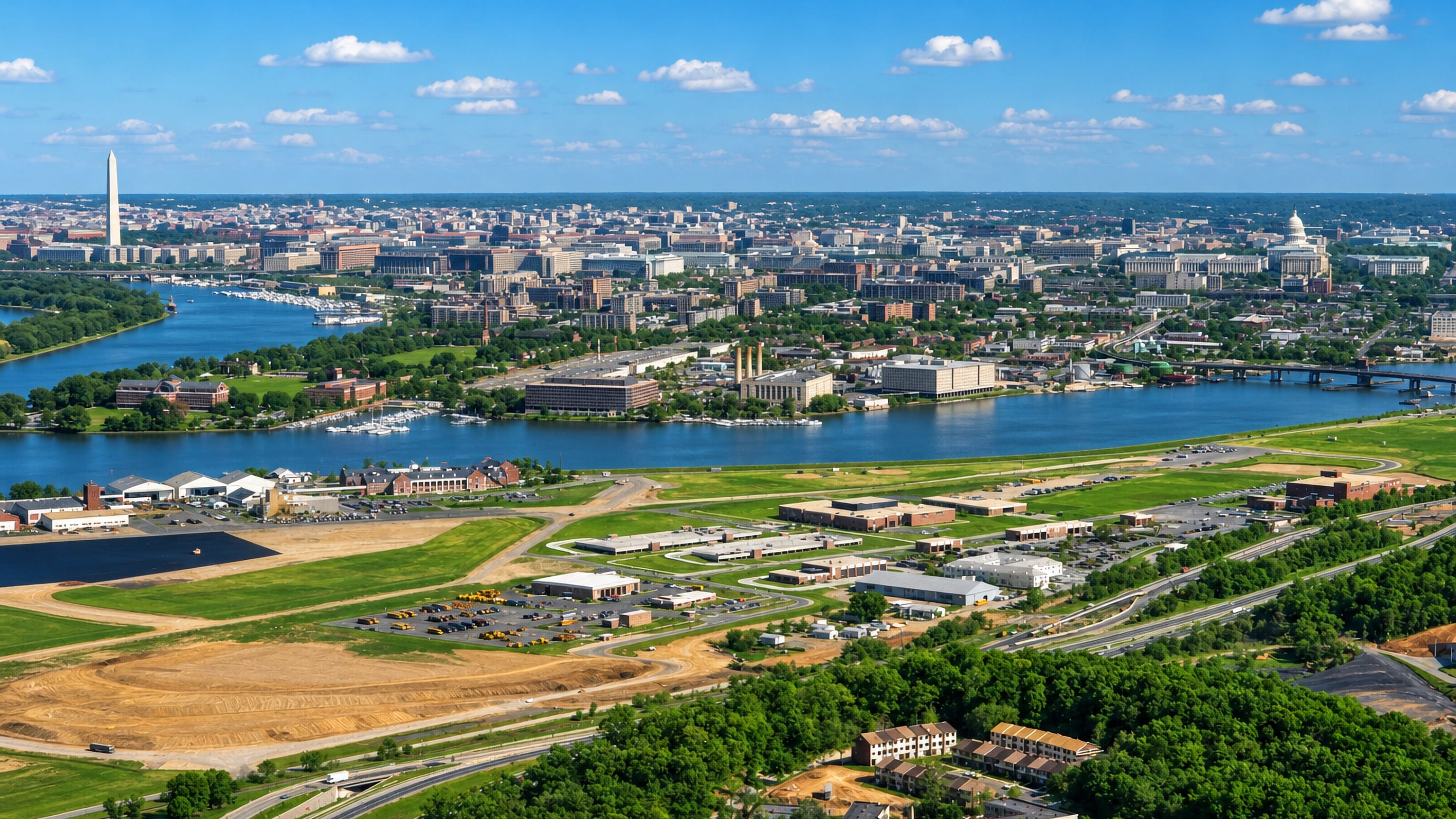 Aerial over Anacostia's riverfront in Washington, DC, with the Washington Monument and Capitol dome beyond.
