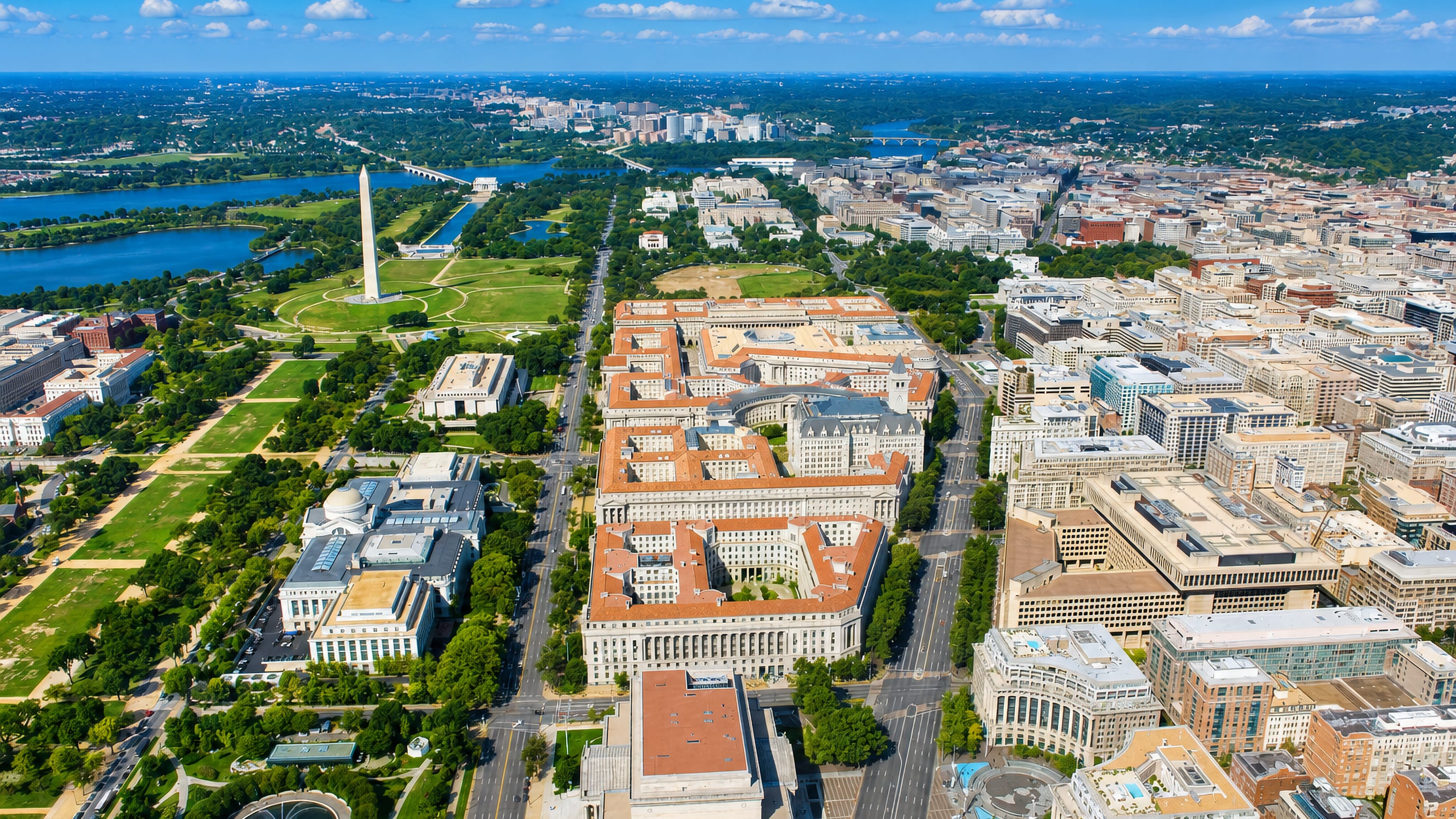 Aerial of the red-roofed Federal Triangle blocks along Pennsylvania Avenue with the Washington Monument beyond.