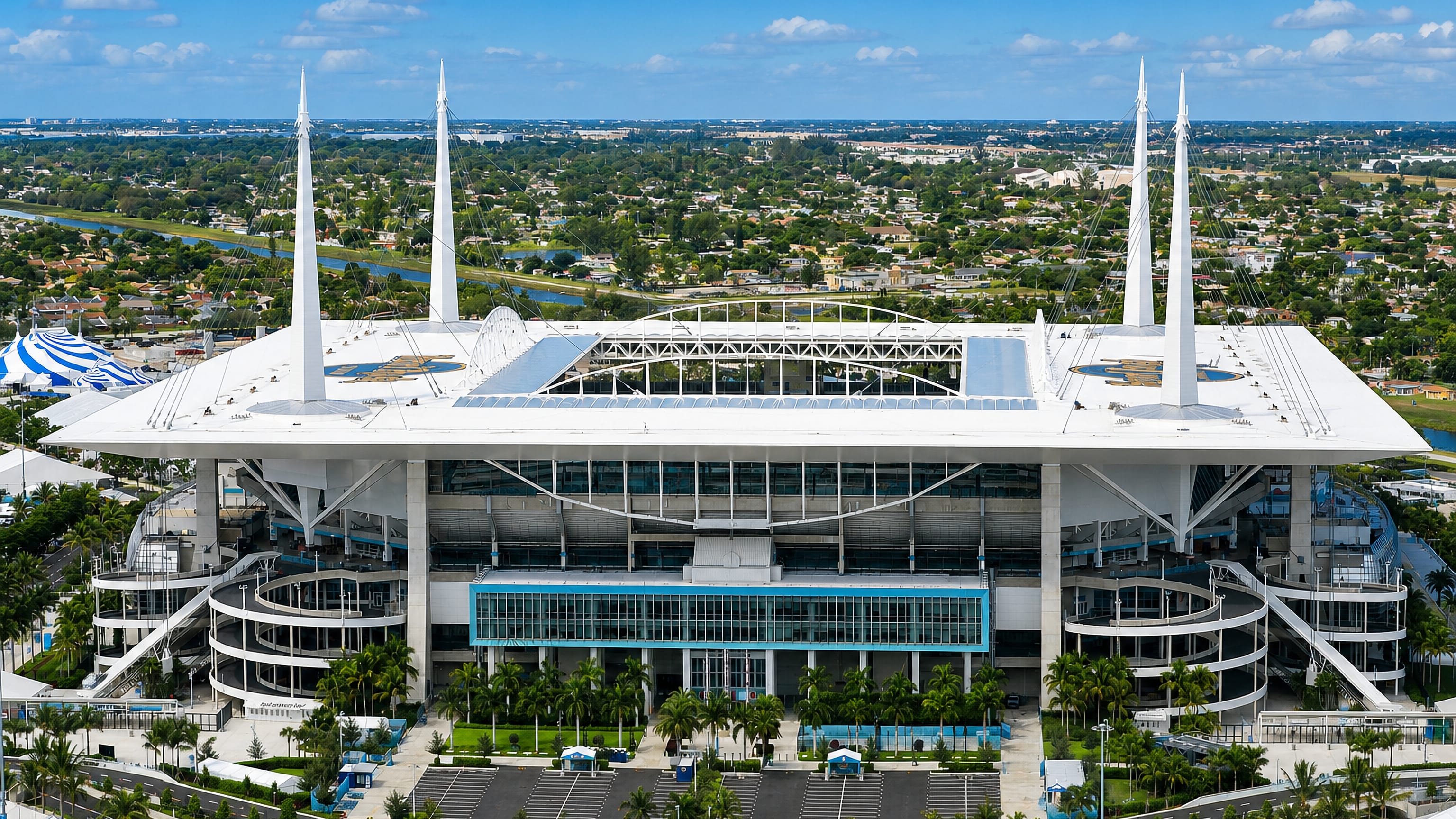 Hard Rock Stadium's white cable-mast canopy rising above the low-rise streets and palms of Miami Gardens, Florida