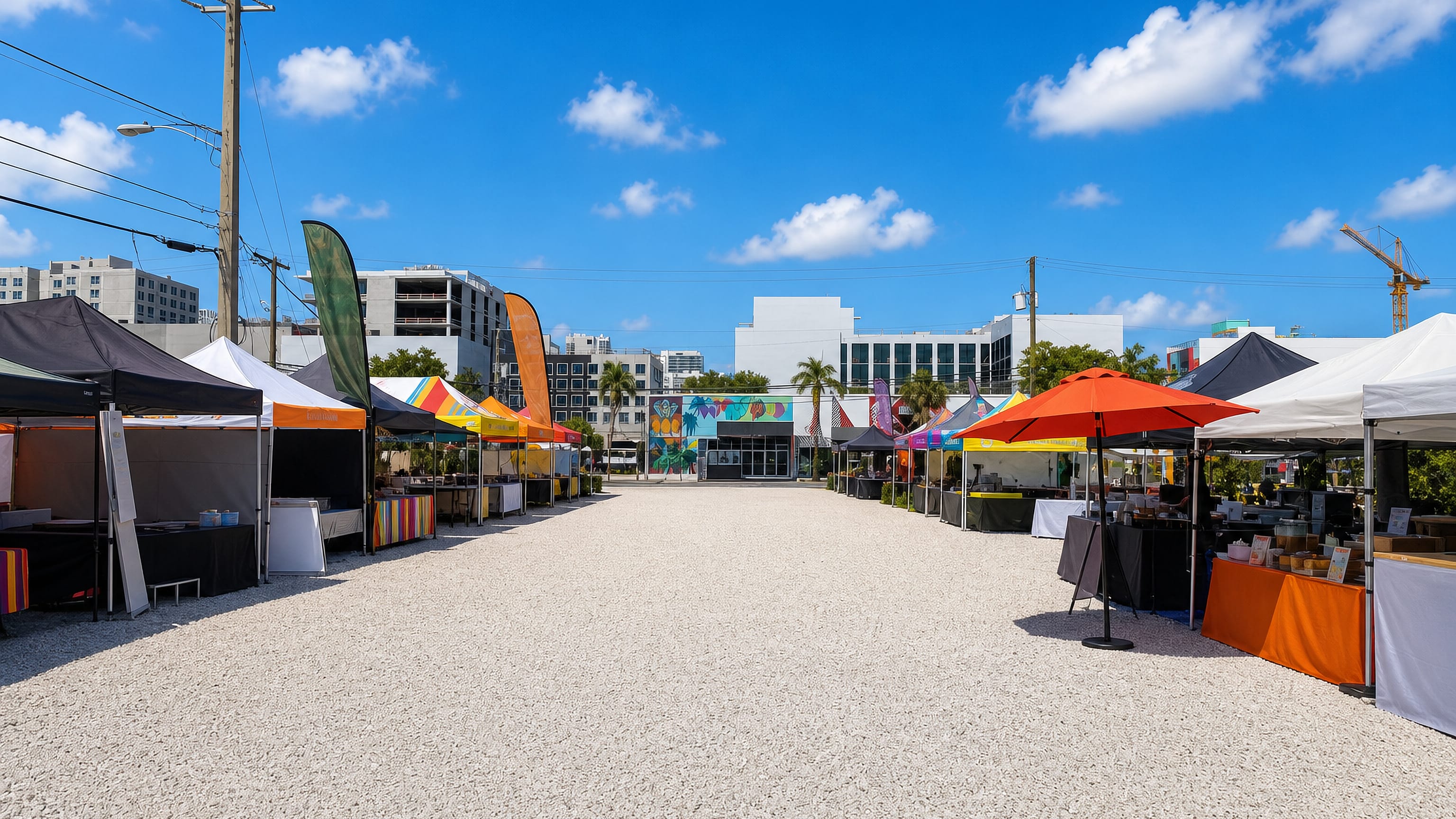 Open-air market stalls under bright canopies facing a mural-painted warehouse in Wynwood, Miami.