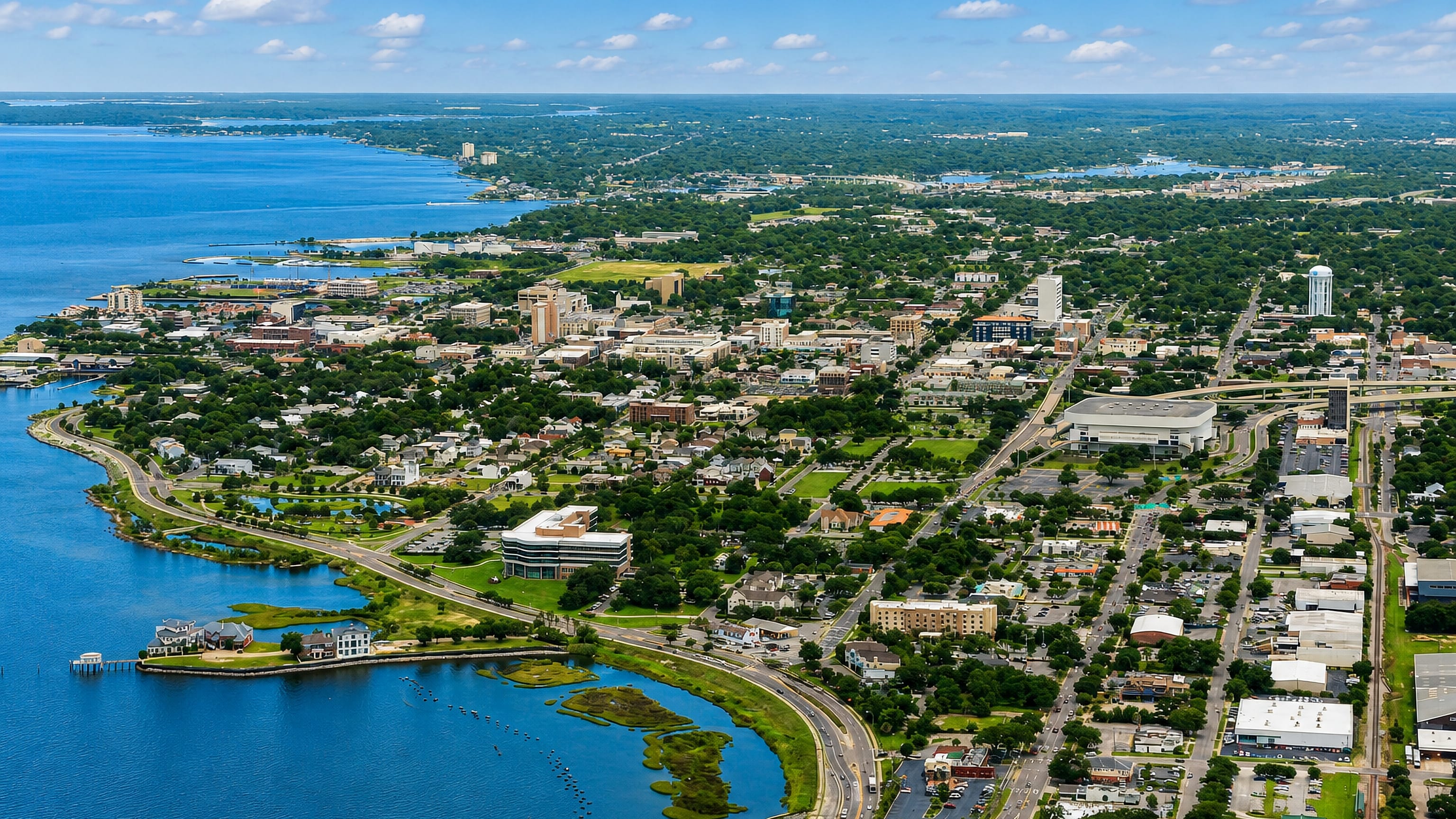 Aerial view of downtown Pensacola, Florida along its bayfront waterfront under a bright blue sky.