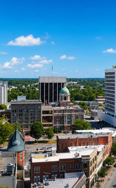 Downtown Macon, Georgia with its green courthouse dome, church steeple and low-rise towers under a blue sky.