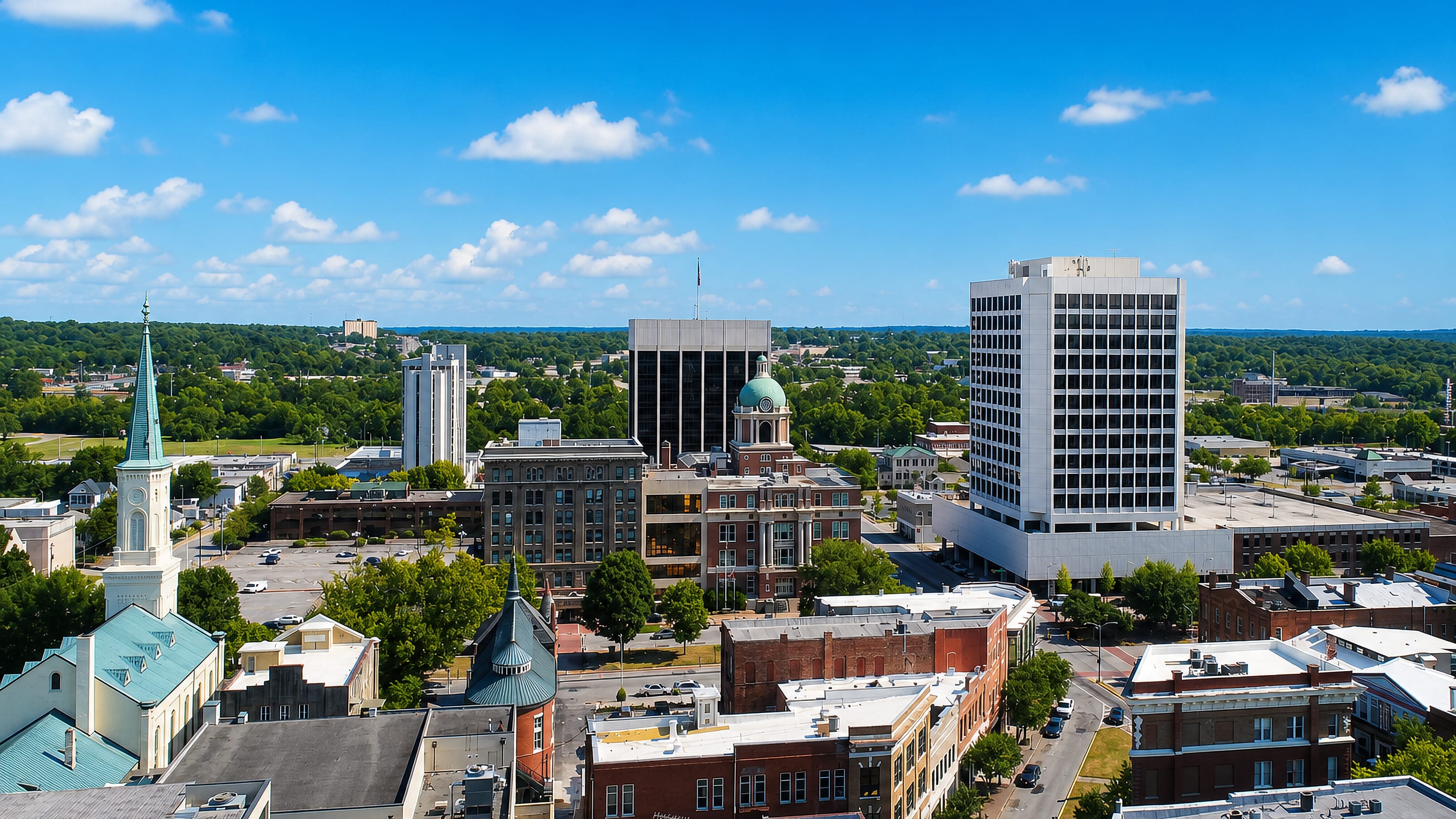 Downtown Macon, Georgia with its green courthouse dome, church steeple and low-rise towers under a blue sky.