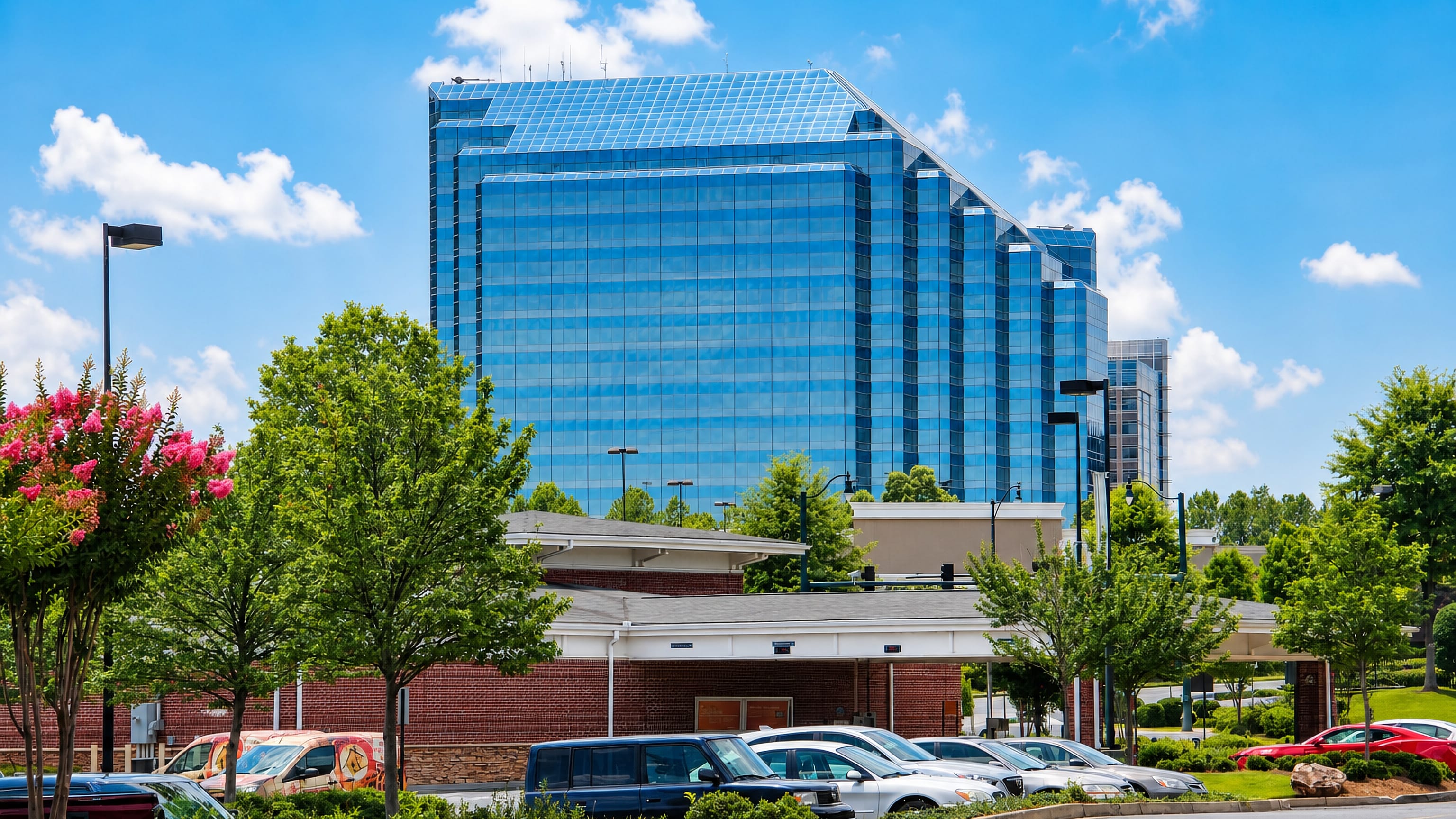 Blue glass office tower rising above low brick buildings and street-level parking in Sandy Springs, Georgia.