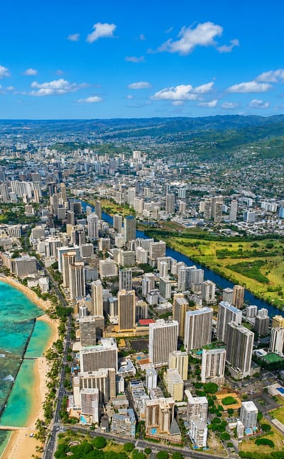 Aerial of Waikiki, Honolulu with beachfront high-rises, turquoise water and Diamond Head crater beyond.