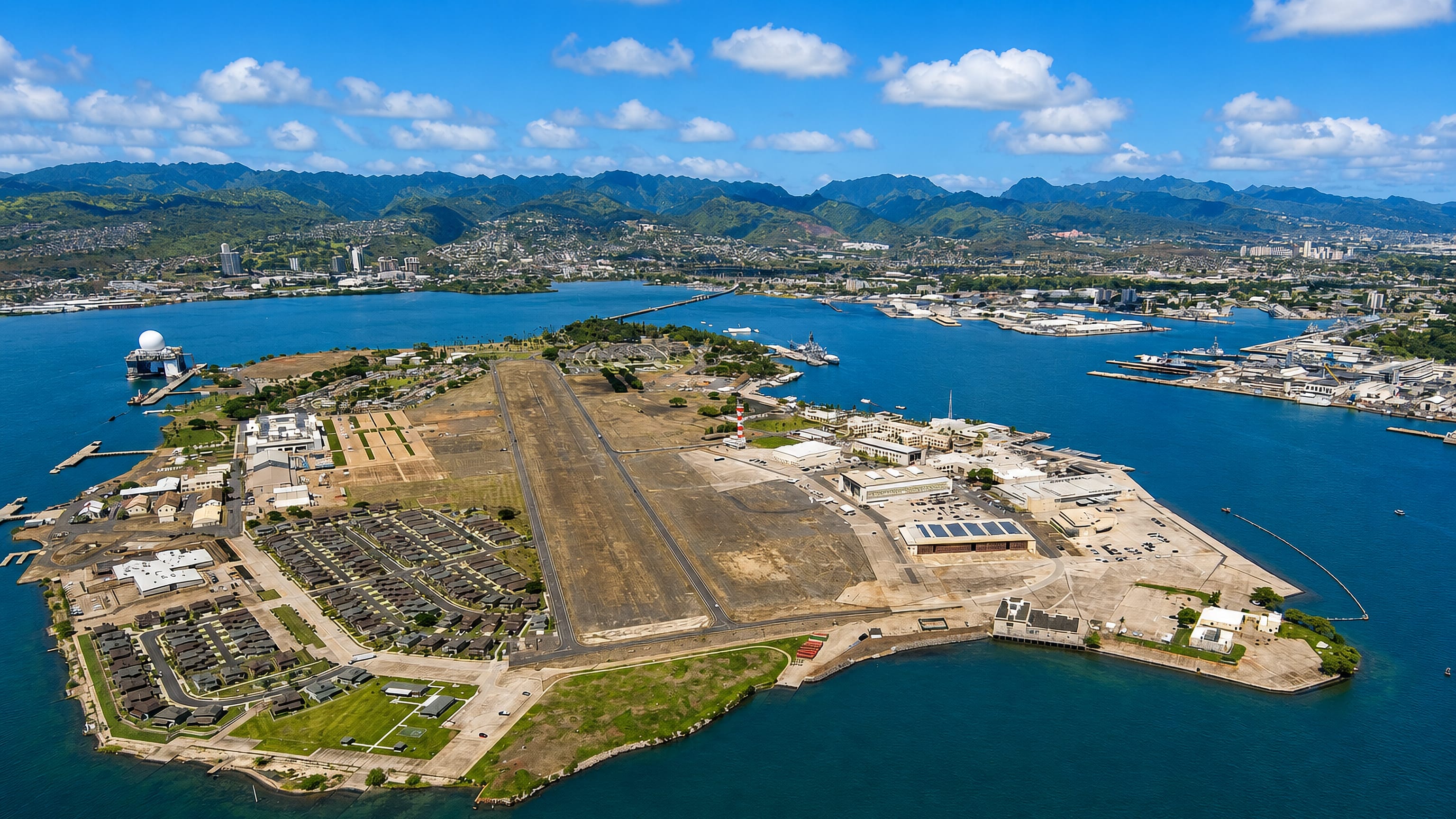 Aerial view of Ford Island in Pearl Harbor, Hawaii, its runway and naval housing ringed by the harbour.