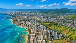 Aerial of Waikiki, Honolulu with beachfront high-rises, turquoise water and Diamond Head crater beyond.