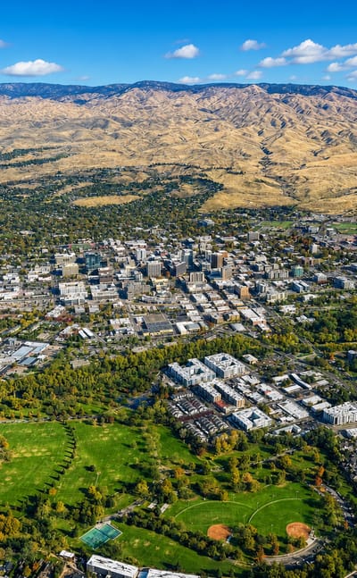 Aerial view of downtown Boise with riverside parks below the tawny Boise foothills.