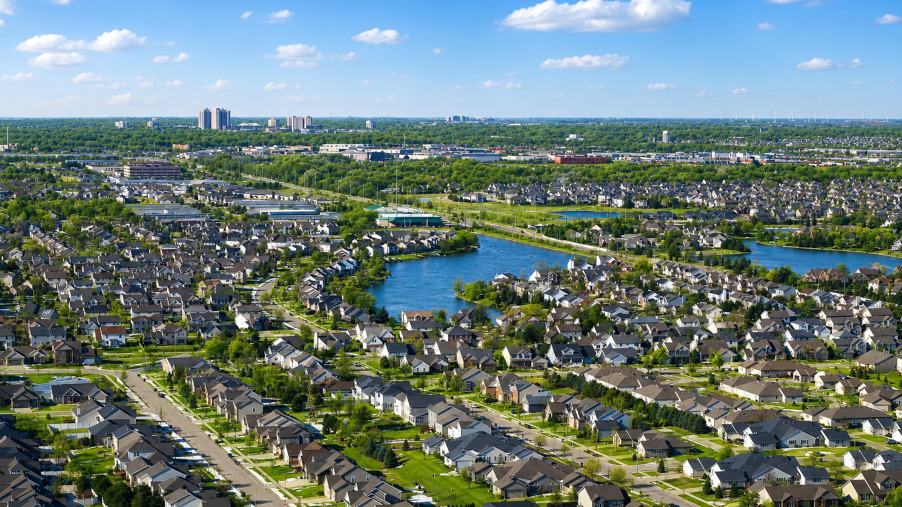 Aerial view over Bloomington, Illinois, with tree-lined suburban streets, small lakes and a distant skyline