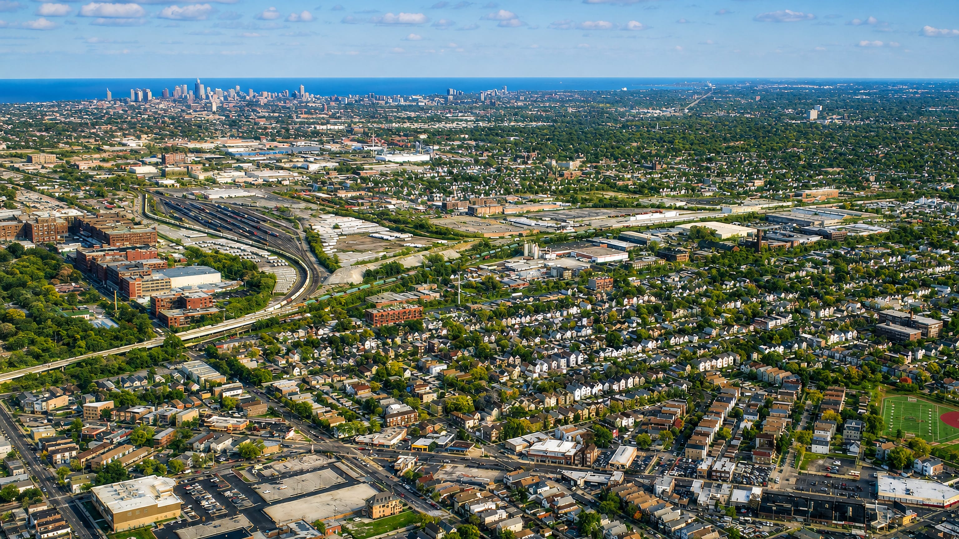 Aerial view over Brighton Park's bungalow grid and rail yards with the Chicago skyline on the horizon.