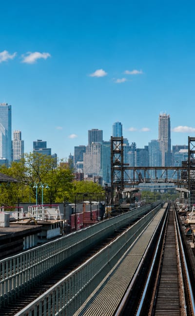 Elevated Chicago "L" train tracks and station platforms leading toward the downtown skyline with the Willis Tower under a clear sky