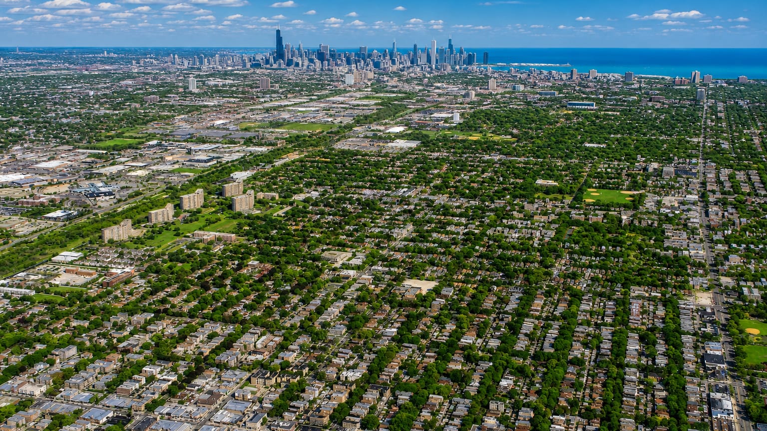 Aerial over the dense residential street grid of West Ridge, Chicago, with the downtown skyline and Lake Michigan on the horizon