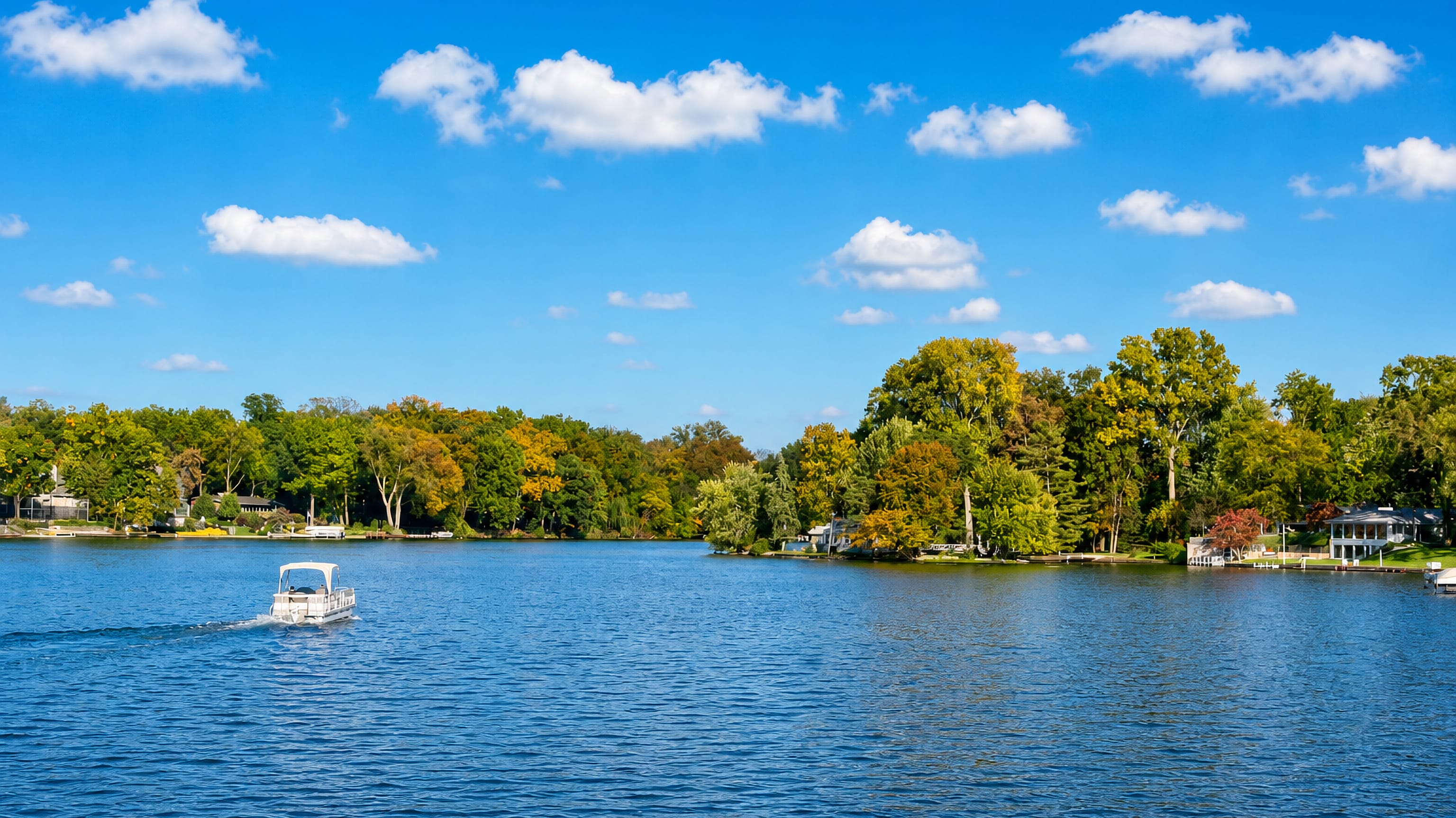 Pontoon boat on a wooded lake fringed with autumn colour and waterfront homes near Elkhart, Indiana.