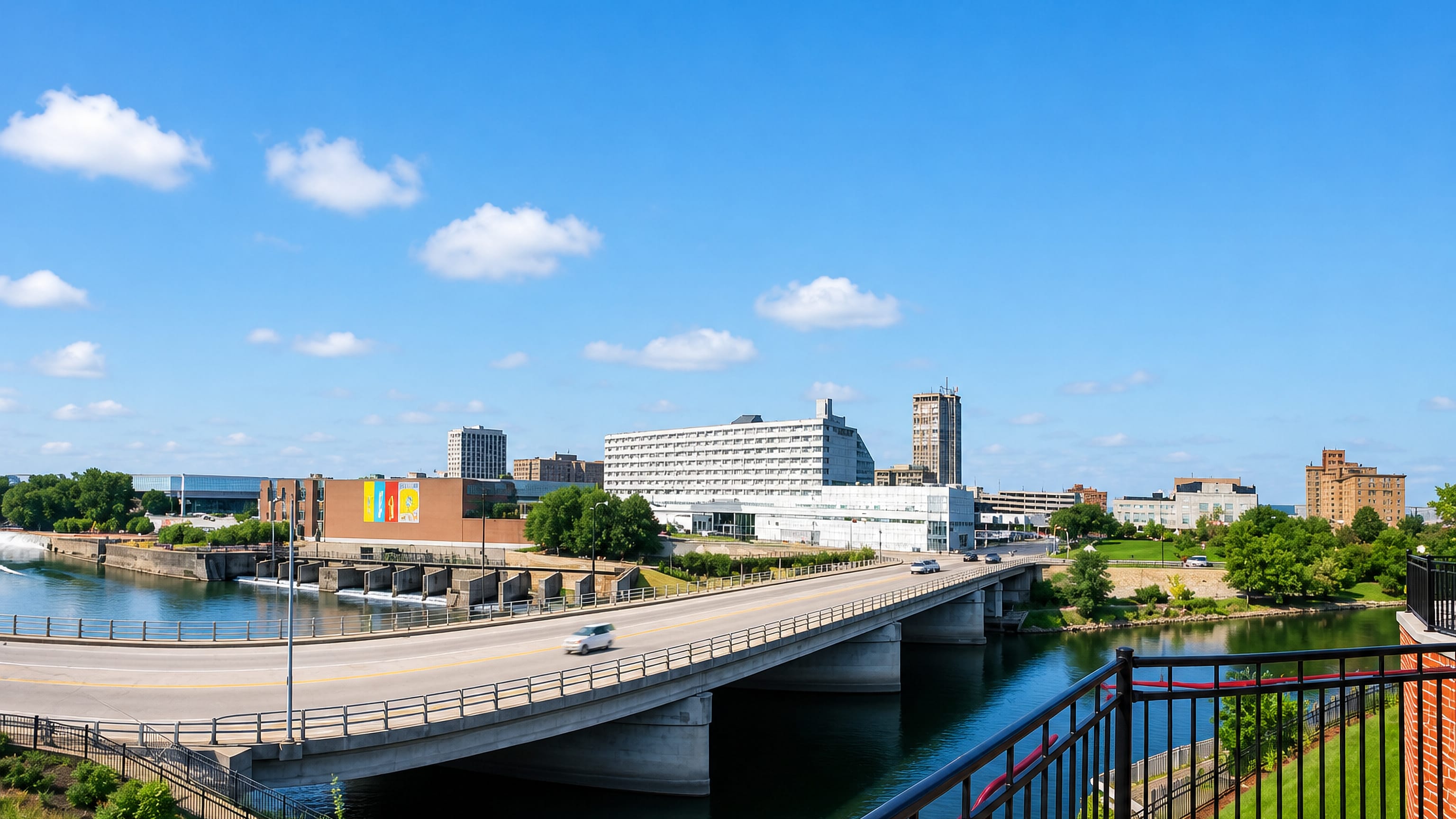 Downtown South Bend rising above the St. Joseph River dam, seen across a wide highway bridge on a clear day