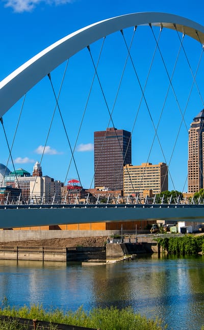 The white arch of the Iowa Women of Achievement Bridge over the Des Moines River with the downtown Des Moines skyline behind