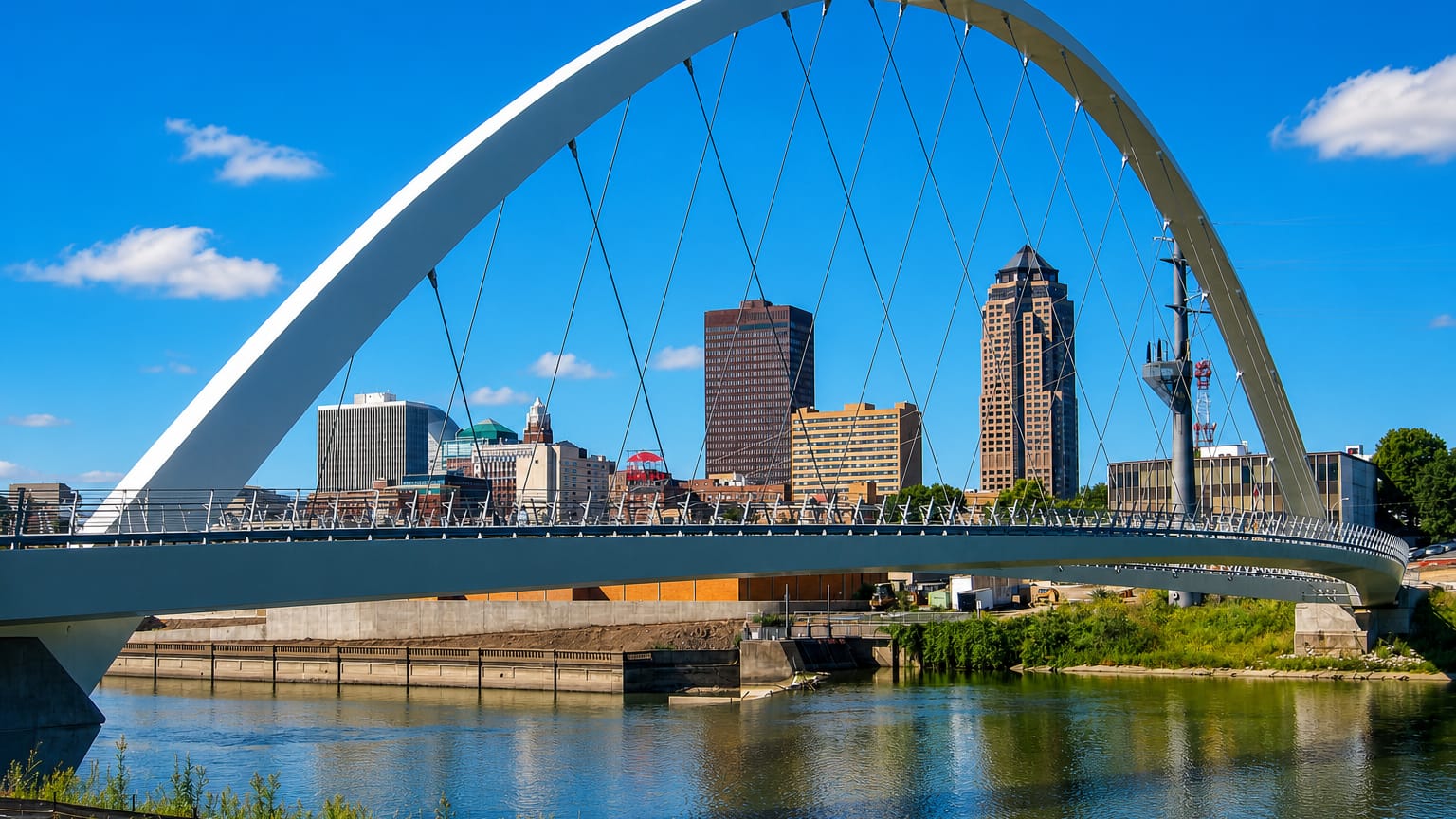 The white arch of the Iowa Women of Achievement Bridge over the Des Moines River with the downtown Des Moines skyline behind